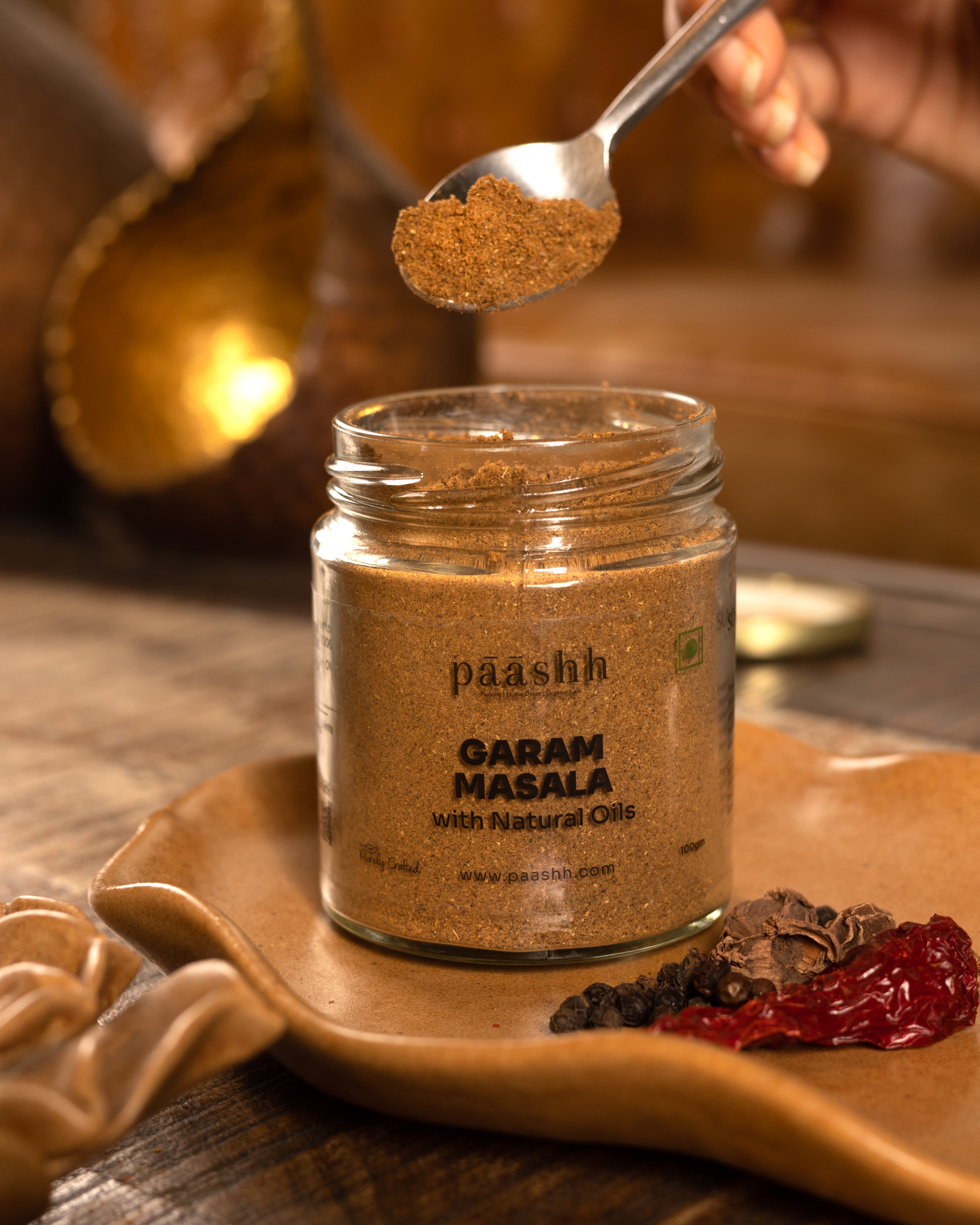 Jar of paashh Garam Masala with a spoonful being poured over it, handcrafted masala blends India, organic kitchen ingredients