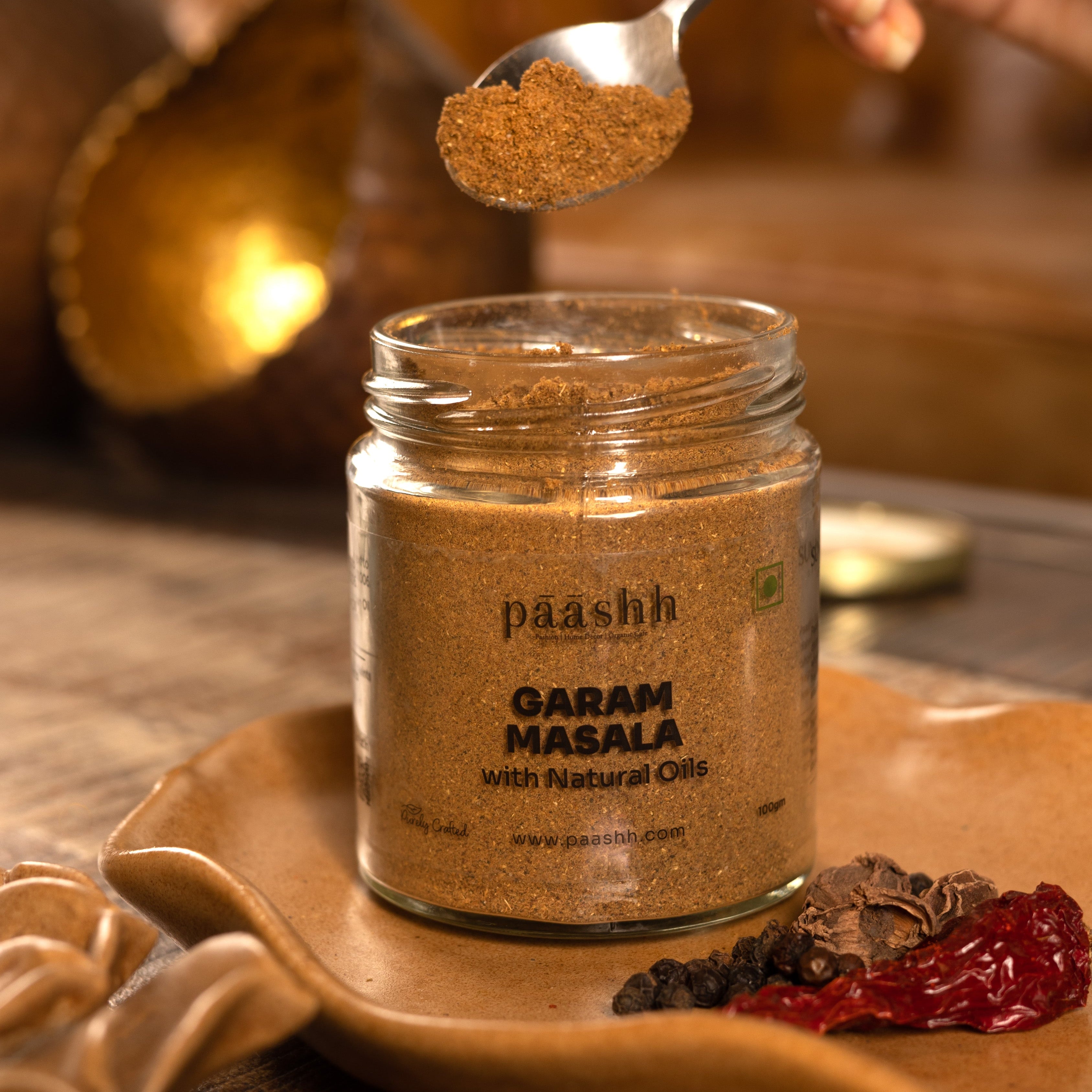 Jar of paashh Garam Masala with a spoonful being poured over it, handcrafted masala blends India, organic kitchen ingredients