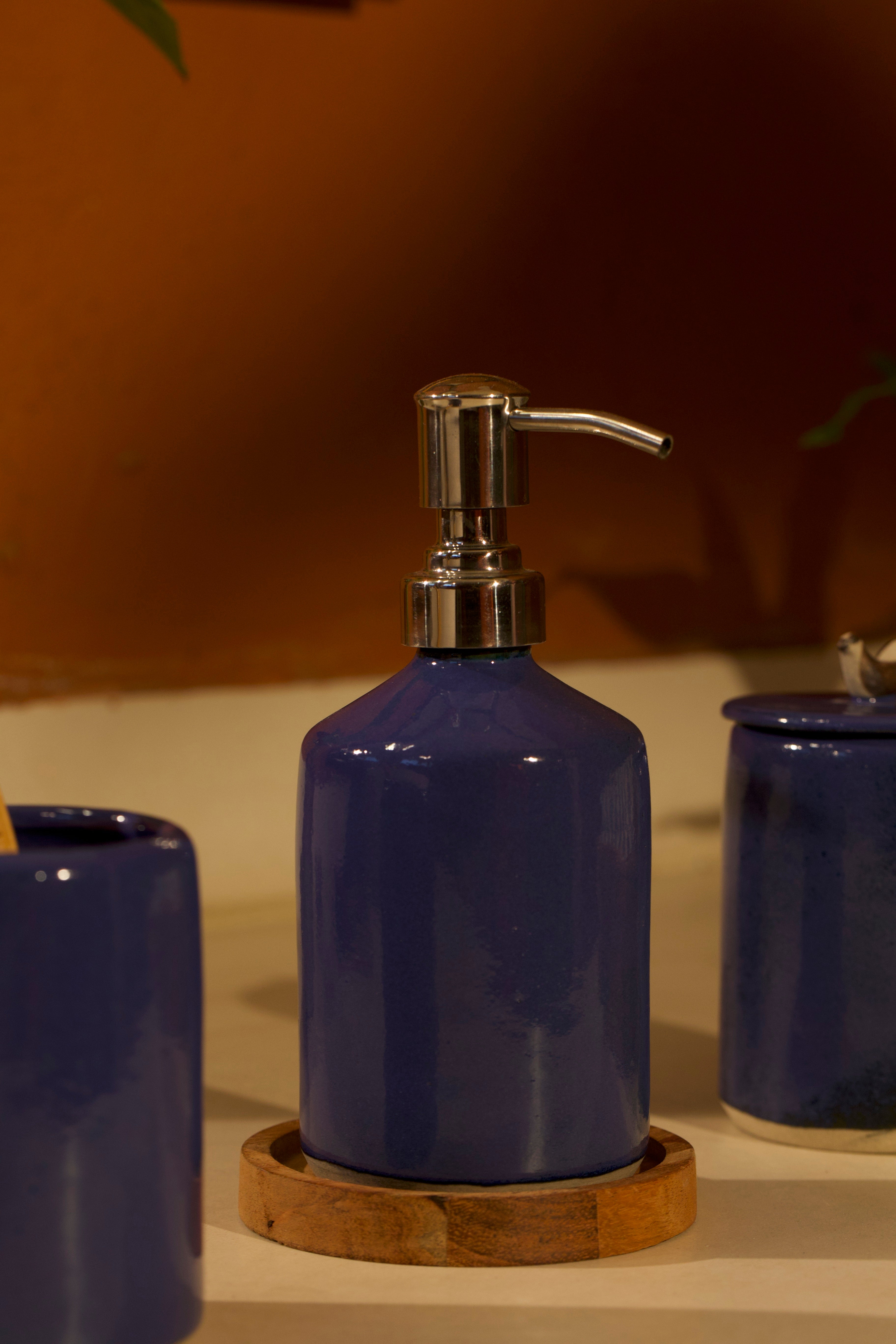 A blue ceramic soap dispenser with silver pump on a wooden coaster. ceramic home décor online, pottery home decor