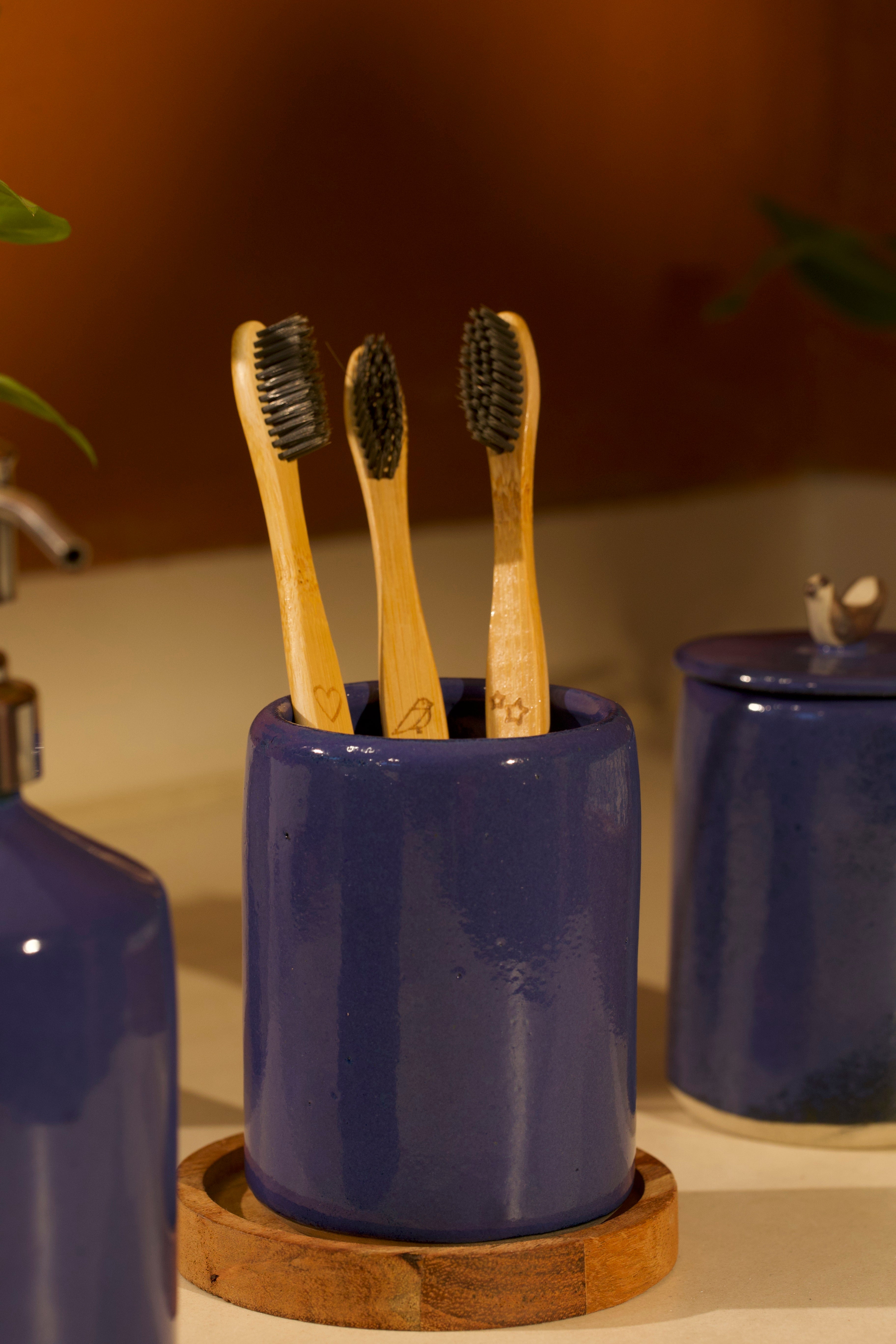 A blue toothbrush holder on a wooden coaster, ceramic home décor online, pottery home decor