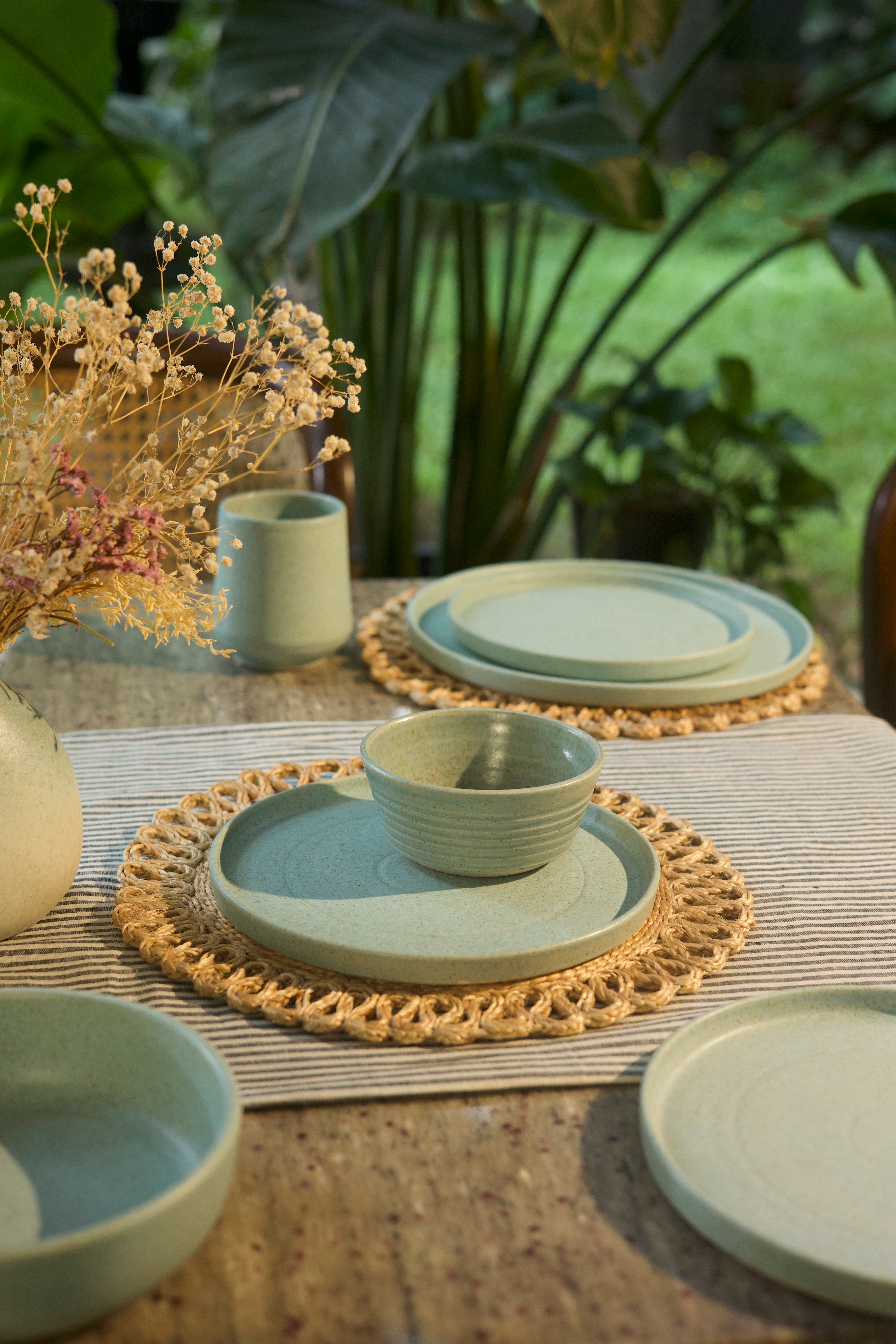 Set of green ceramic plates and bowls on a table with woven placemats, handmade dinnerware India, handcrafted plates and bowls