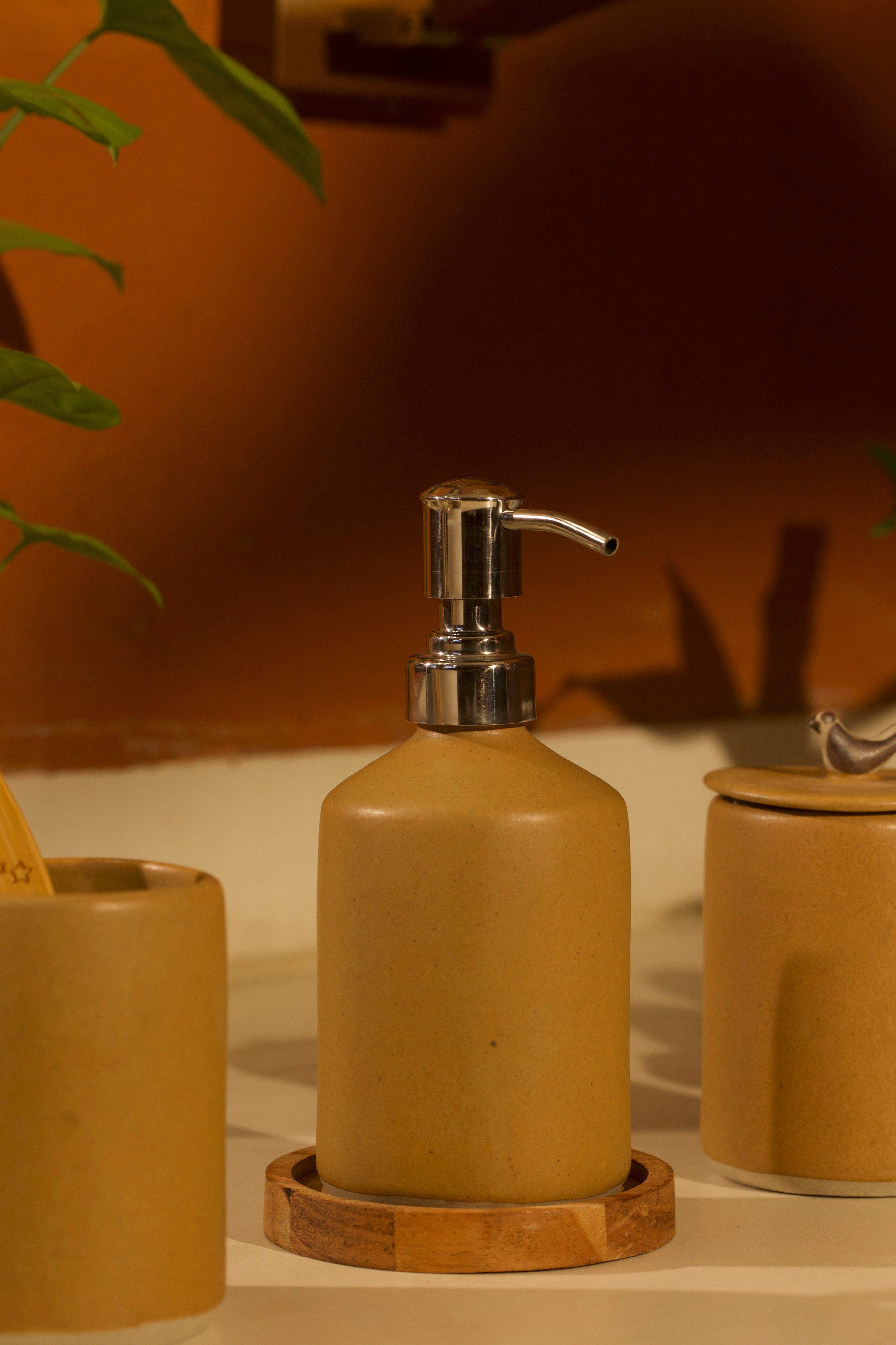 A yellow ceramic soap dispenser with pump on a wooden coaster, ceramic home décor online, pottery home decor