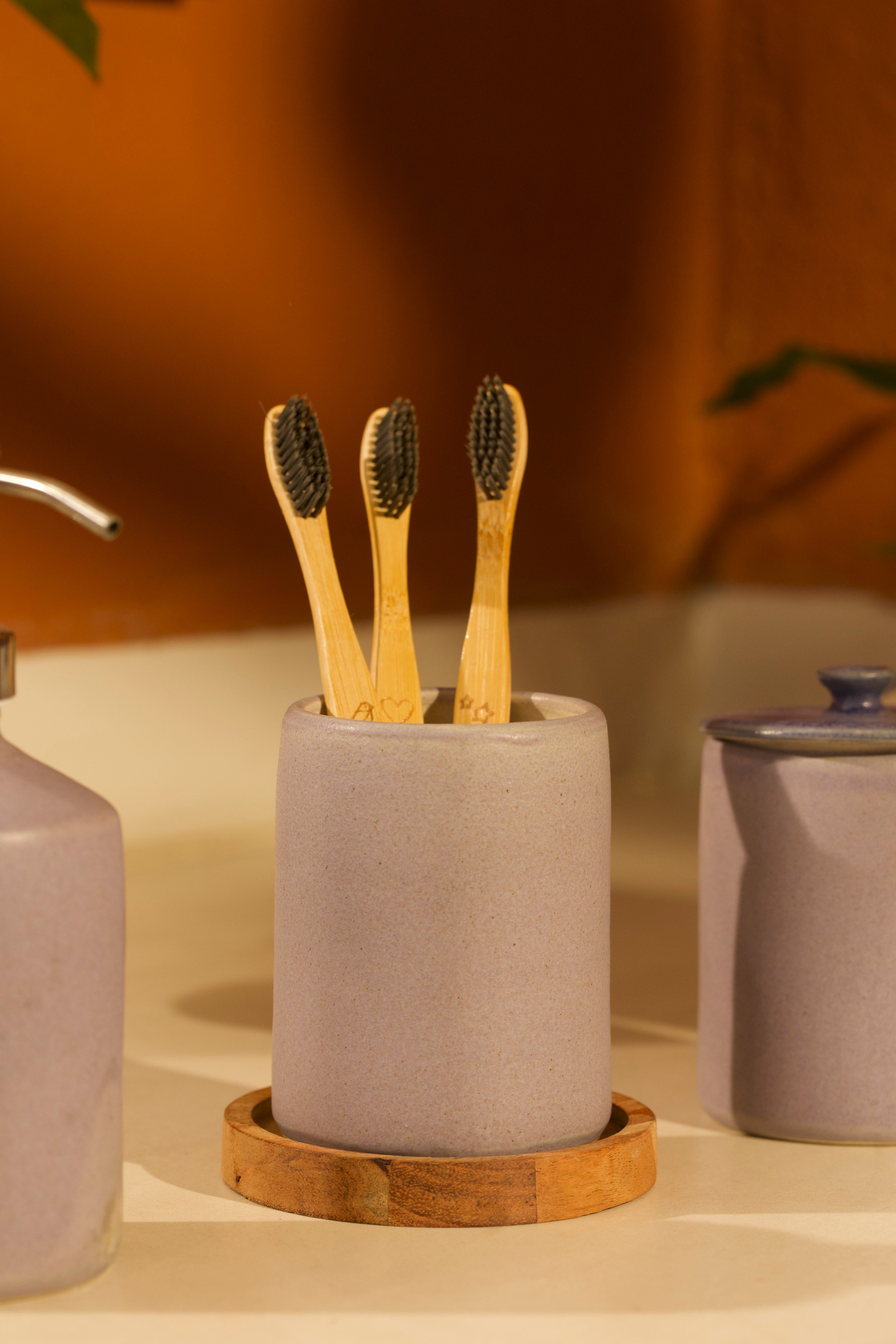 A pink ceramic toothbrush holder on a wooden coaster. ceramic home décor online, pottery home decor