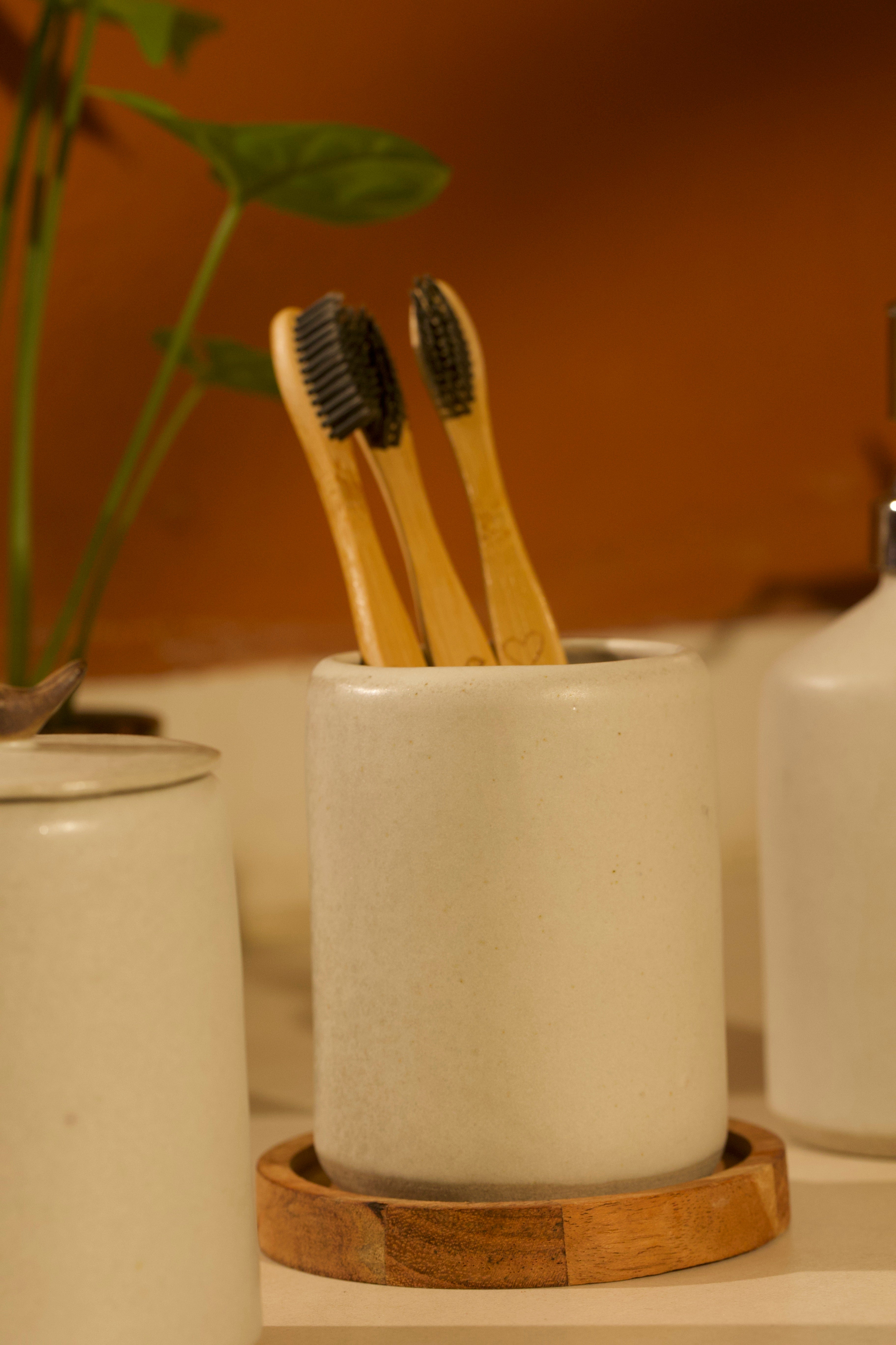 A white ceramic toothbrush holder on a wooden coaster. ceramic home décor online, pottery home decor
