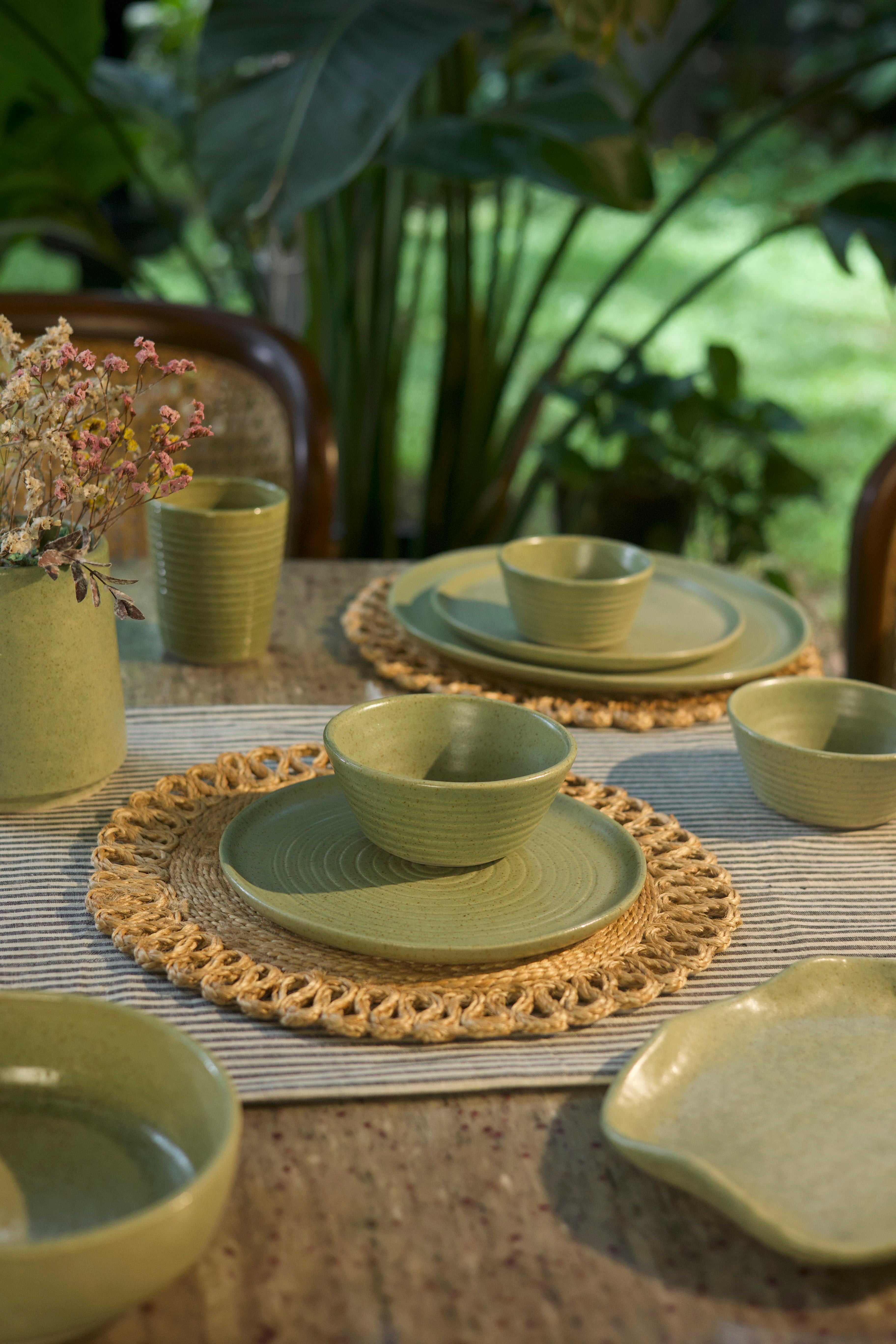 Green ceramic tableware set on a textured surface handmade dinnerware India handcrafted plates and bowls