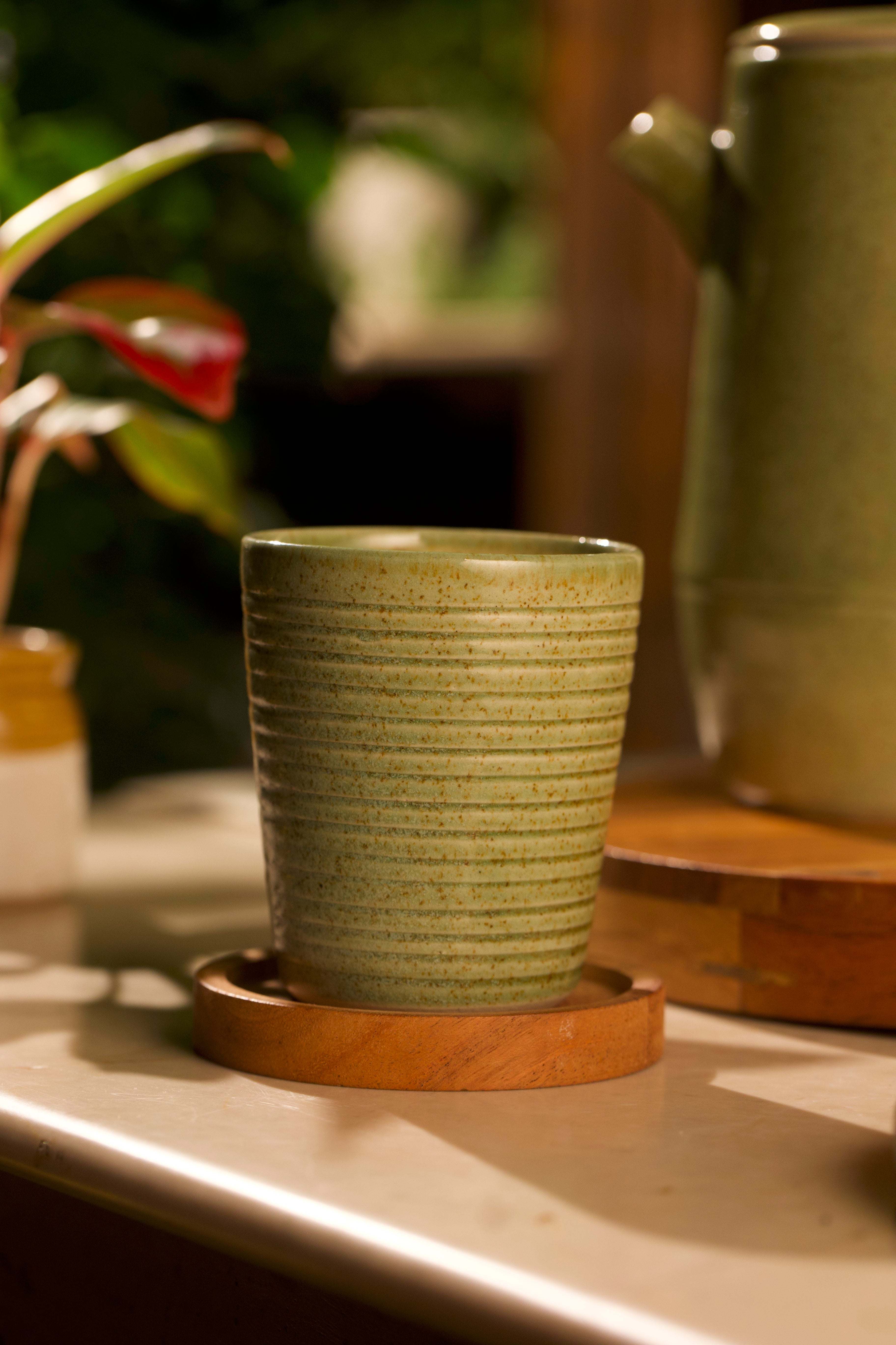 Green ceramic cup on a wooden coaster with a blurred background, artisanal serveware India, handmade ceramics India