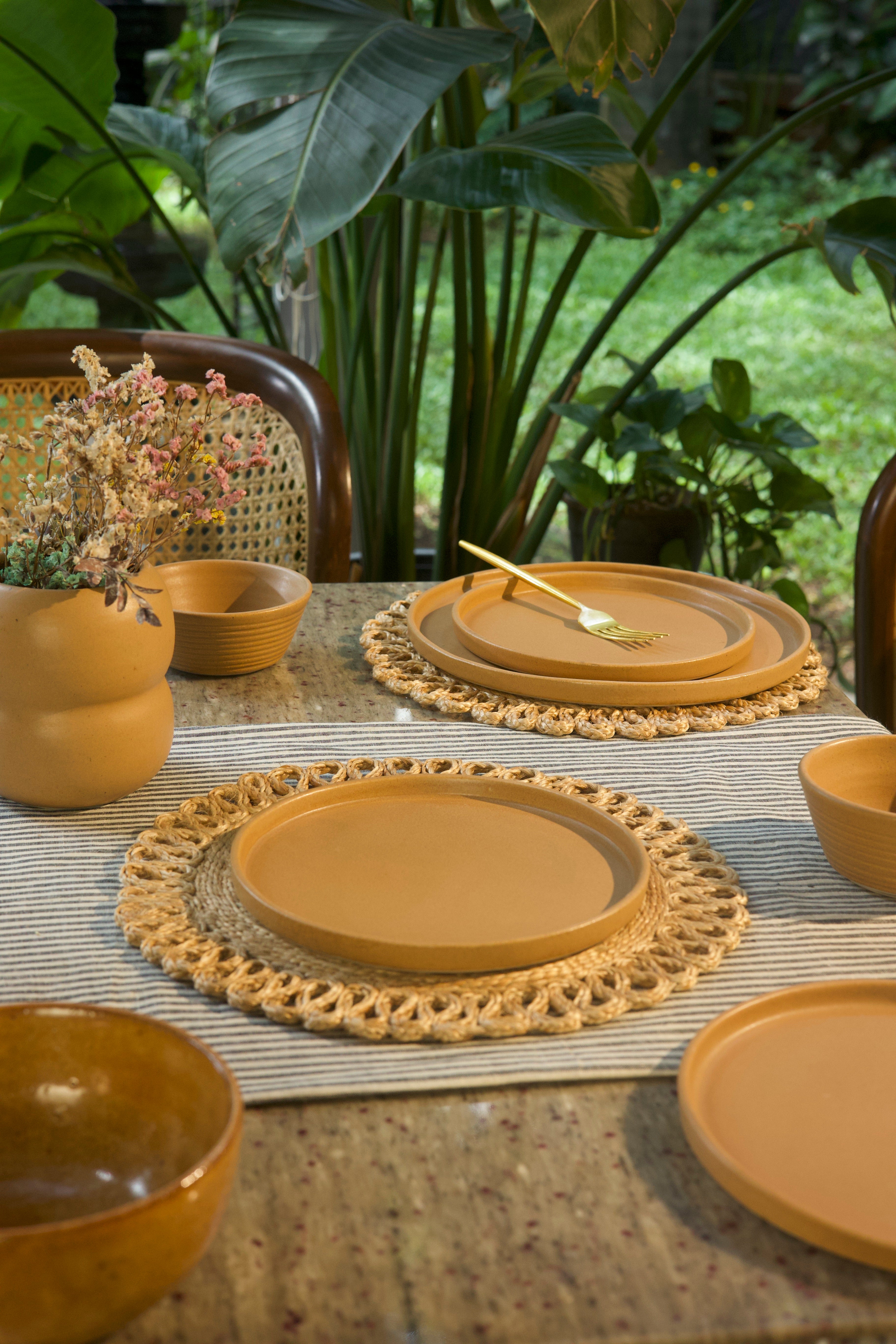 Yellow ceramic plates and bowls on a table with a woven placemat, handmade dinnerware India, handcrafted plates and bowls