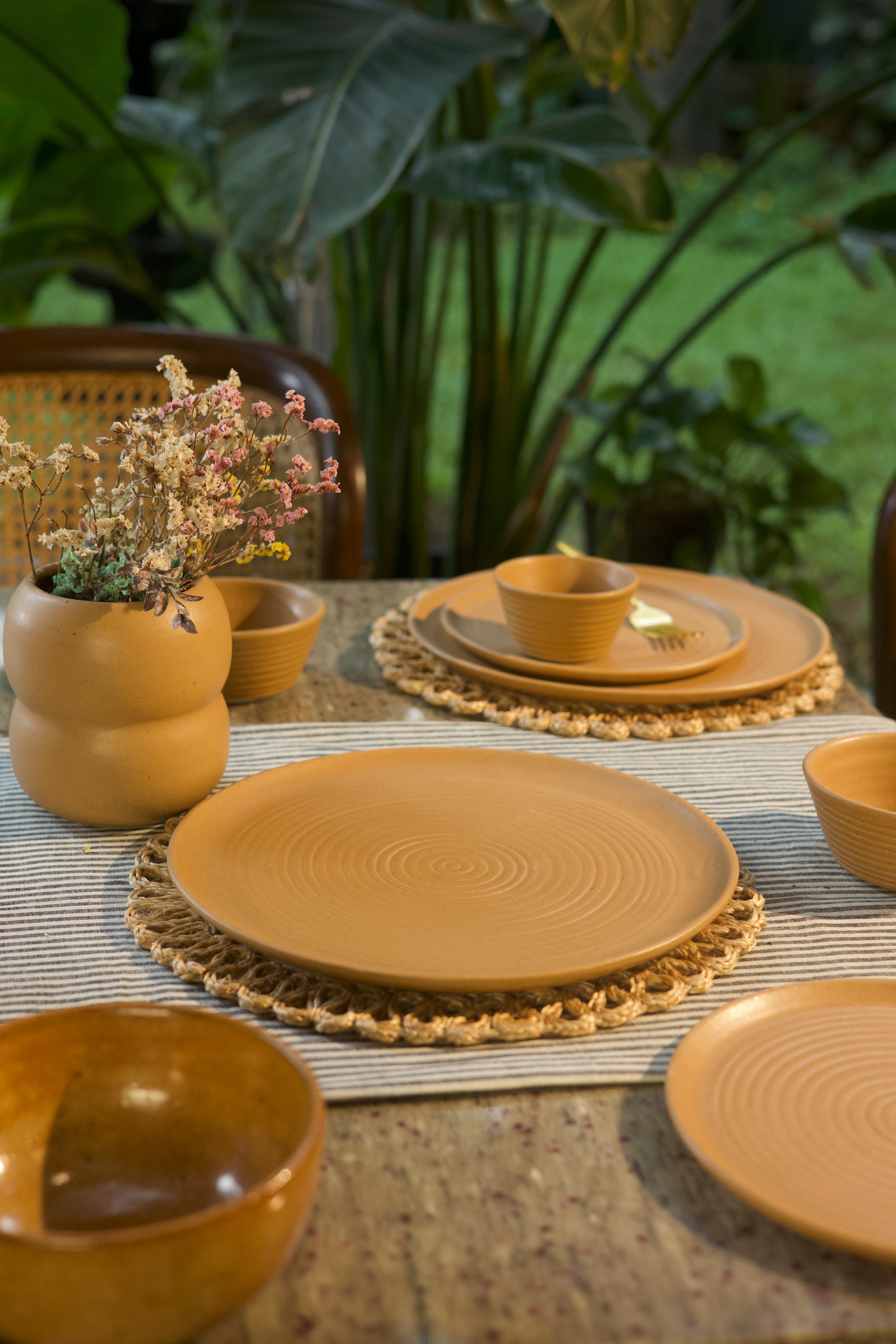 Mustard ceramic tableware set on a textured surface handmade dinnerware India, handcrafted plates and bowls