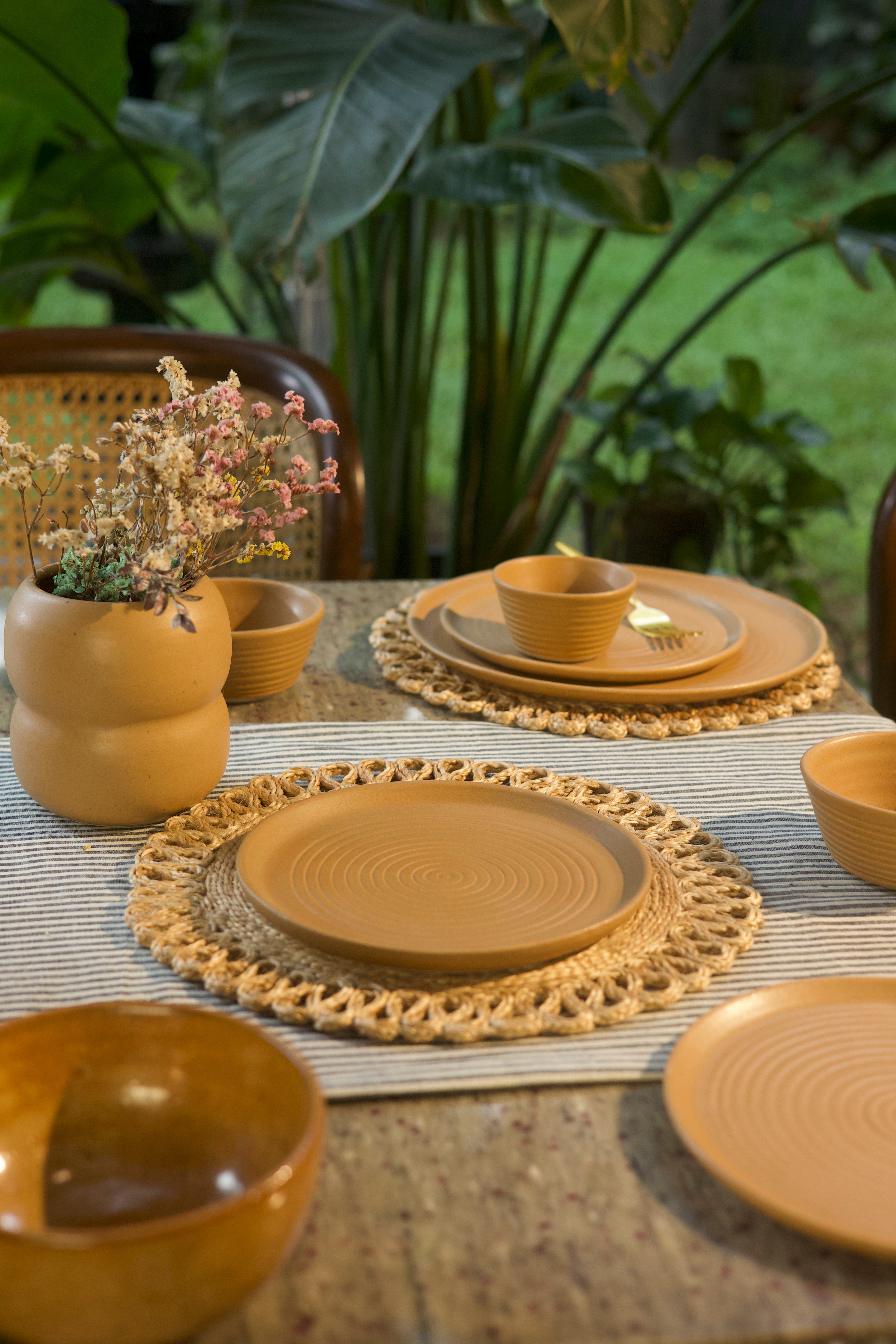 Mustard ceramic plates and bowls on a table with woven placemats, ceramic tableware India, handcrafted plates and bowls