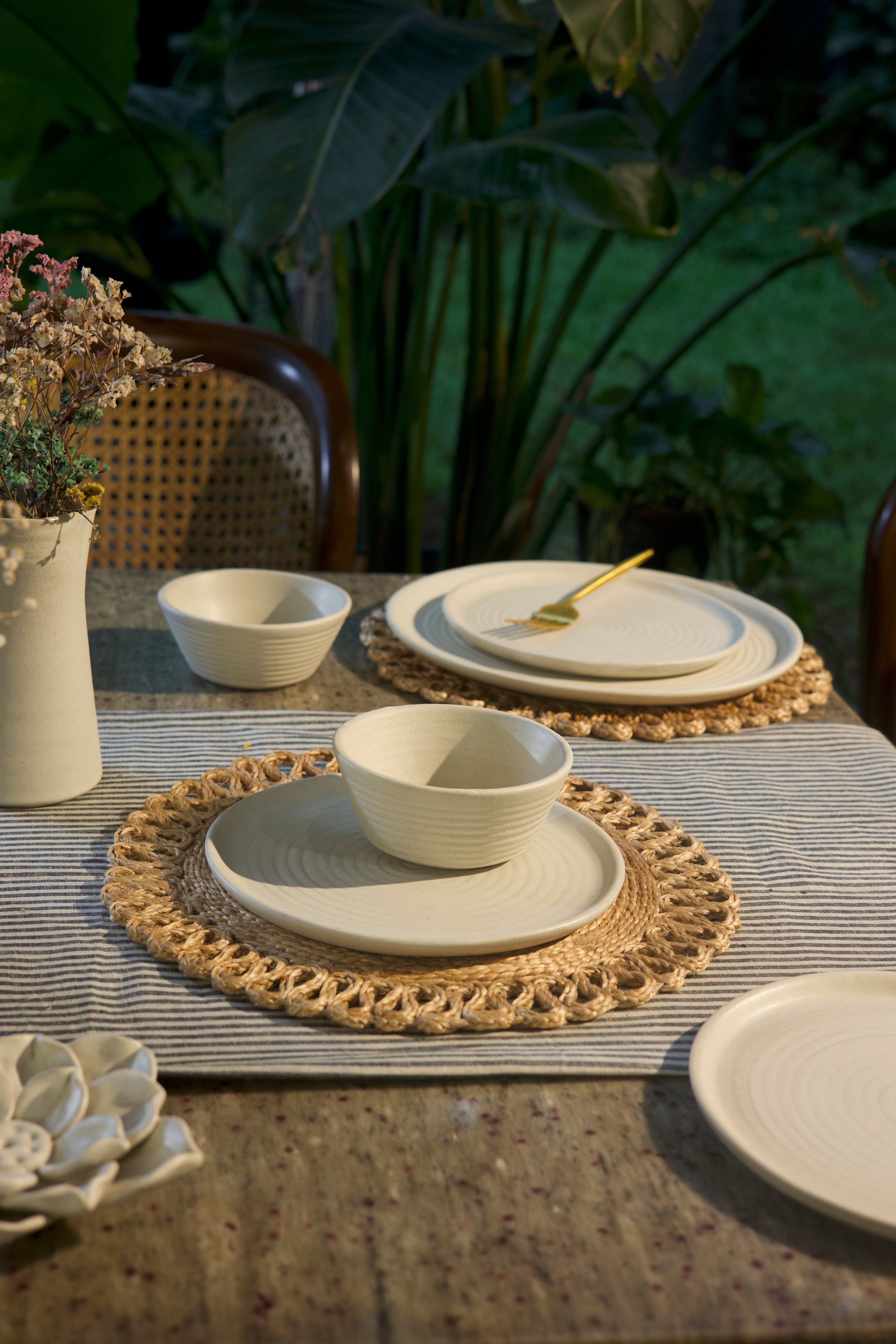 White ceramic tableware on a textured surface, handmade dinnerware India, handcrafted plates and bowls