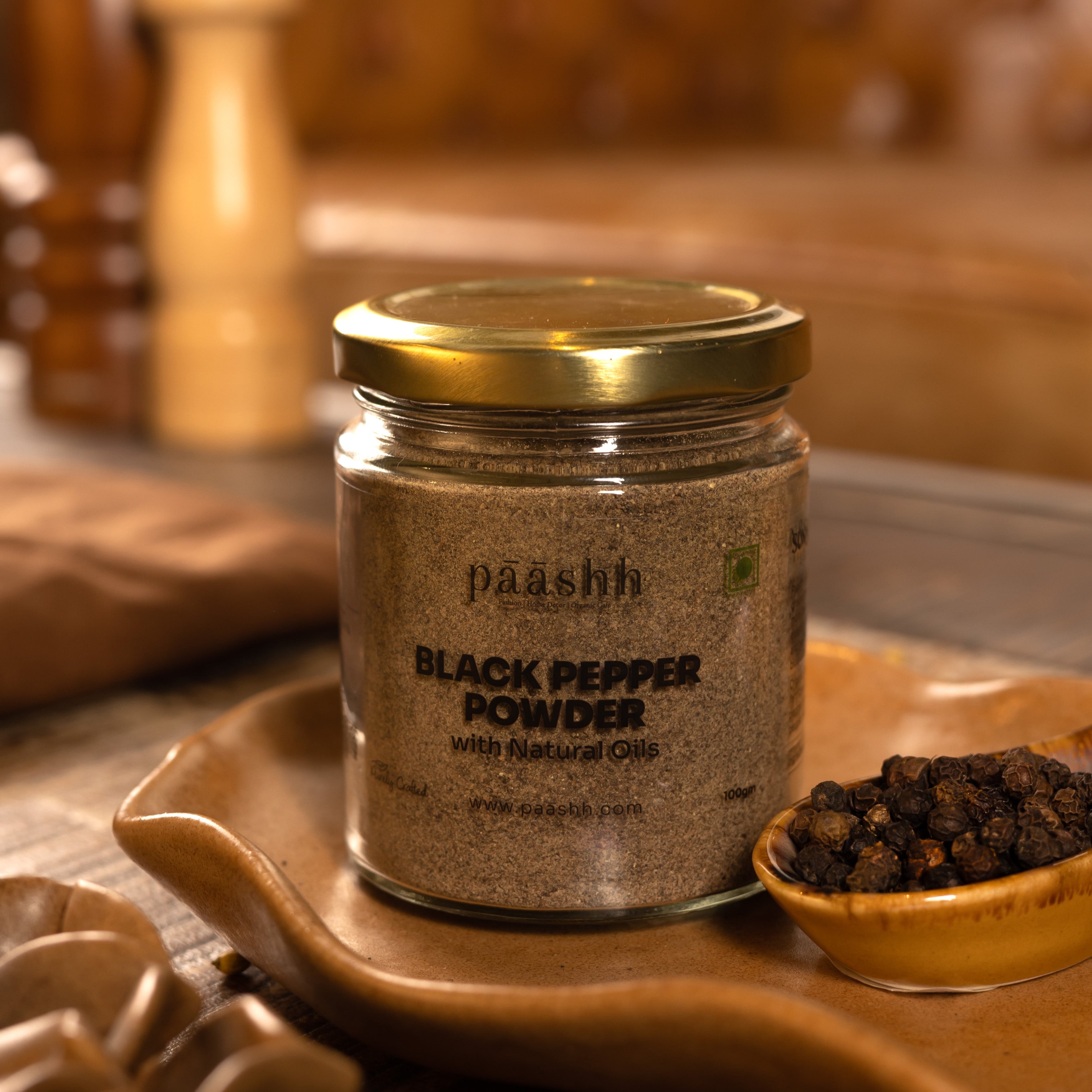 Jar of black pepper powder with a gold lid on a wooden surface, organic spices India, organic kitchen ingredients