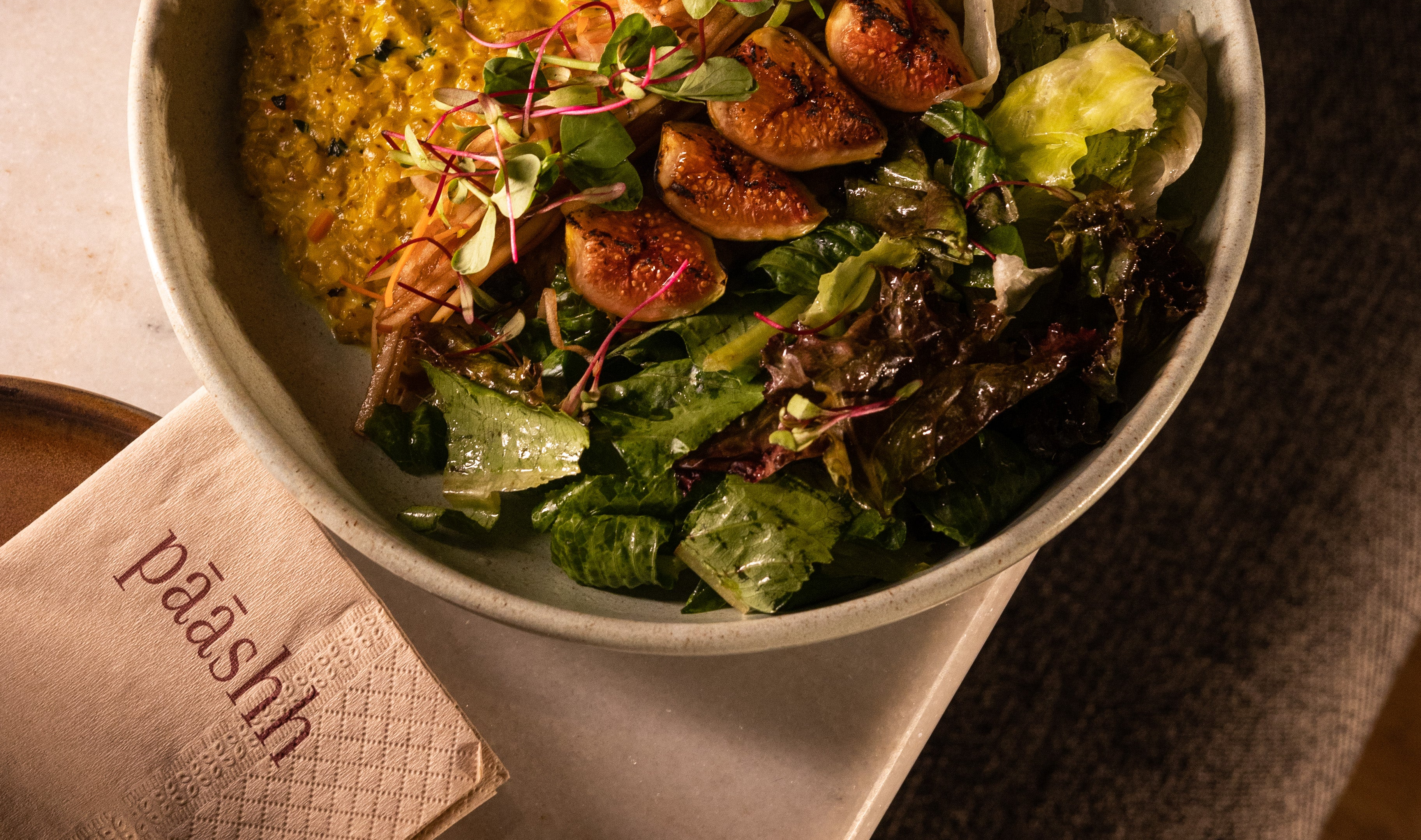 Bowl of salad with figs and greens on a wooden table with 'paashh' napkin,  organic food restaurants in India,
 sustainable dining experiences,
 healthy food places Mumbai