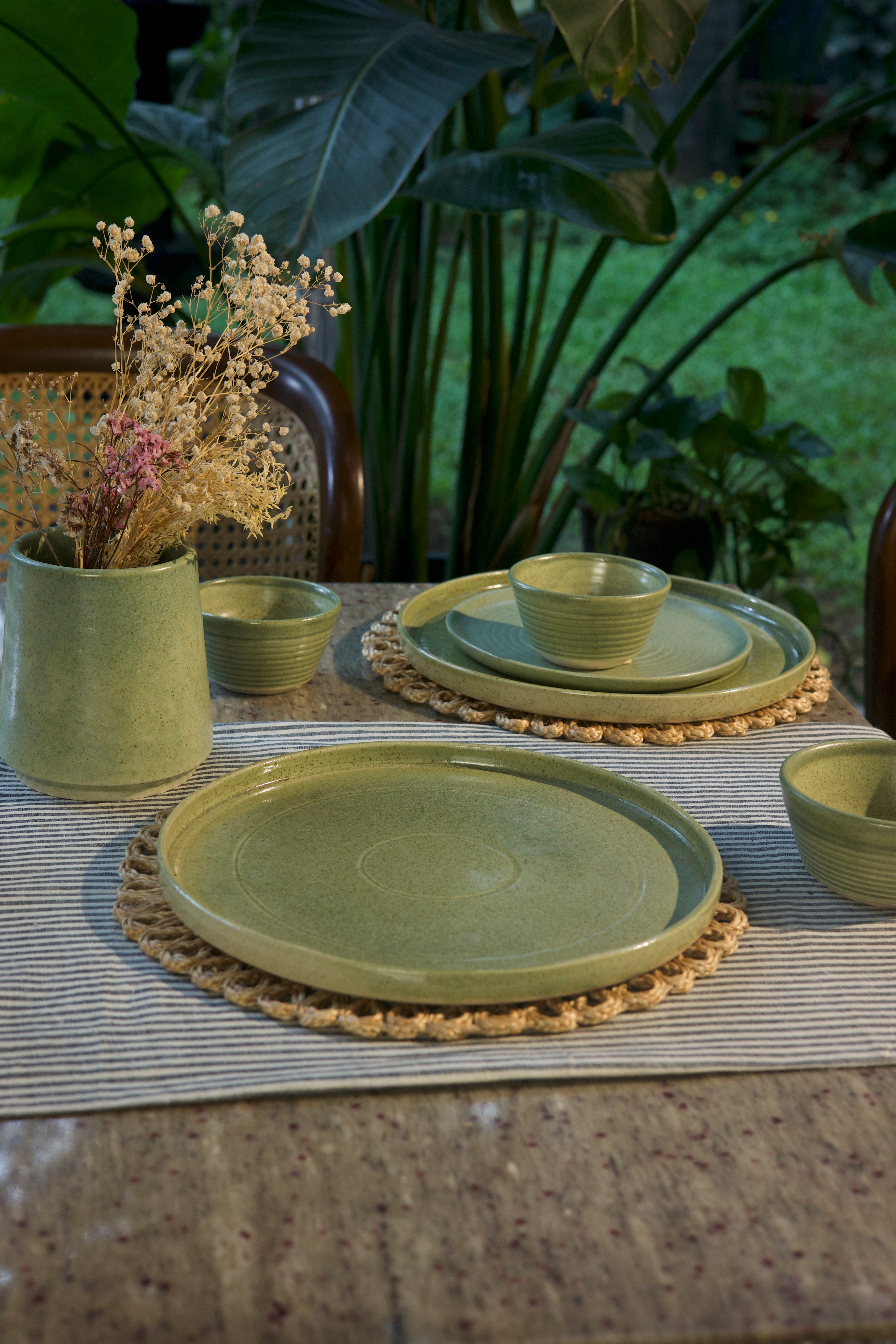 Green ceramic tableware set on a textured surface with plants in the background, ceramic tableware India, handcrafted plates and bowls