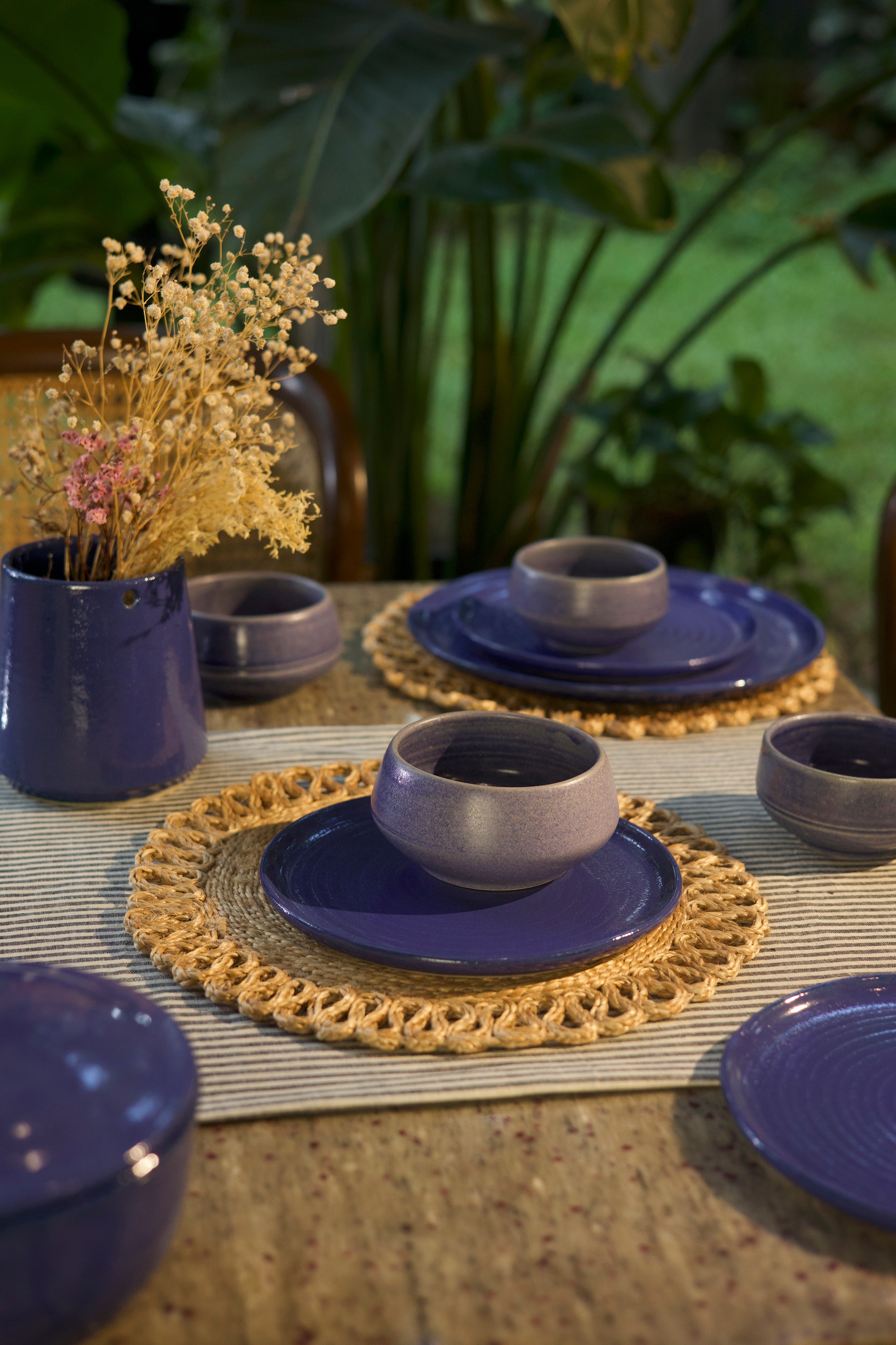 Set of blue ceramic dishes with gold placemats on a table with plants in the background, handmade dinnerware India
 handcrafted plates and bowls