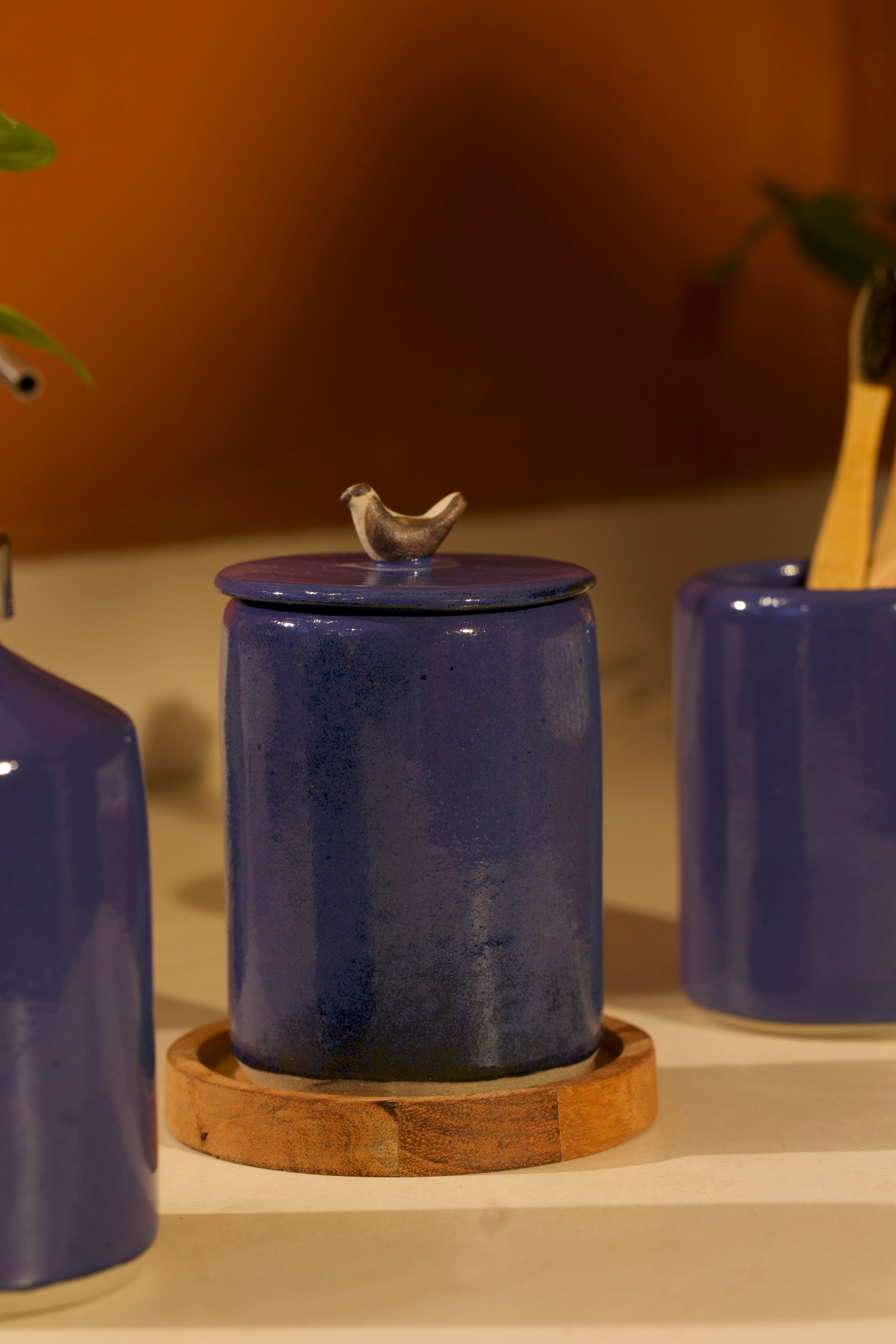 Blue ceramic jar with a bird-shaped finial on a wooden coaster.  ceramic home décor online, pottery home decor