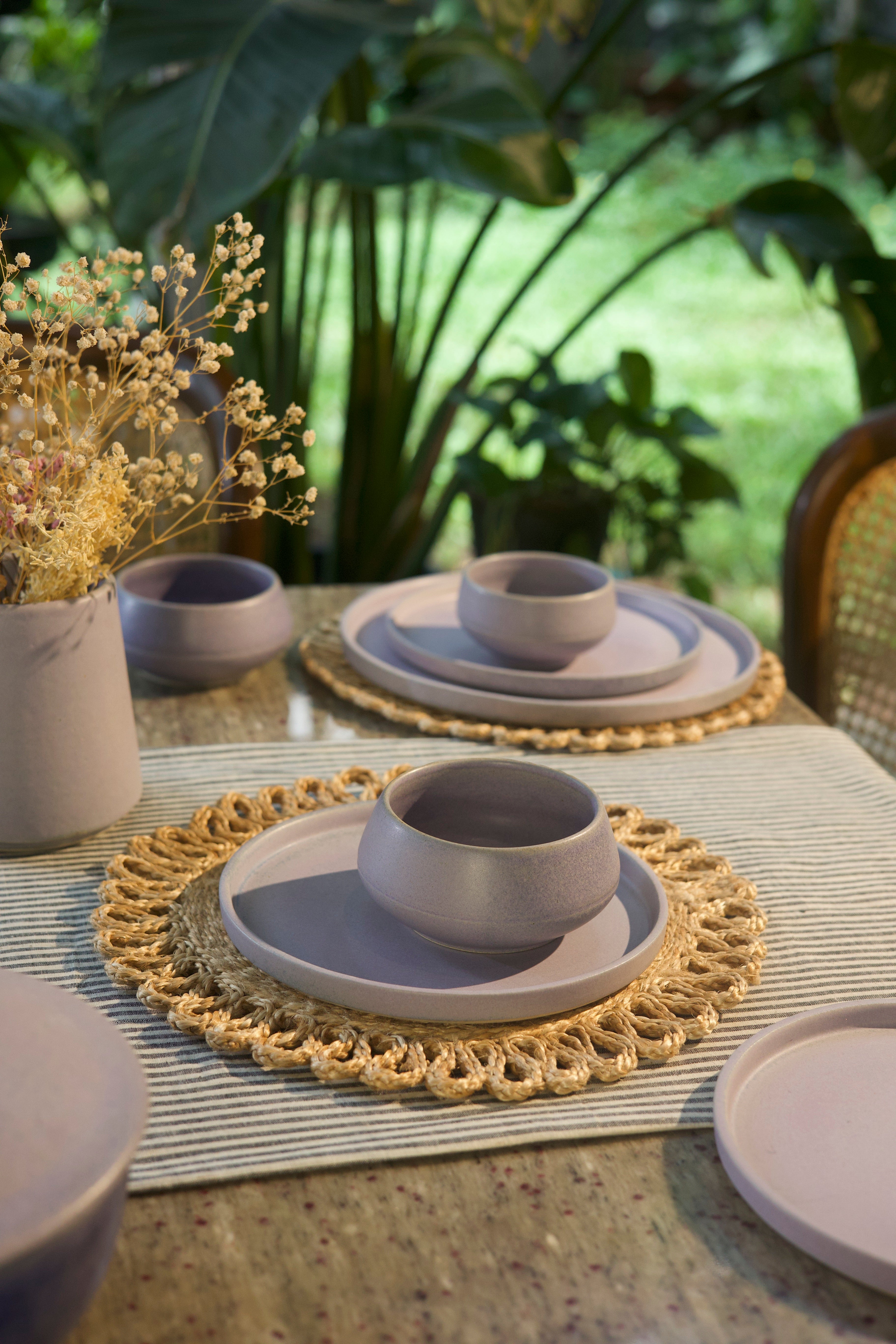 Dining table setting with ceramic bowls and plates on a textured placemat, outdoors. handmade dinnerware India, handcrafted plates and bowls