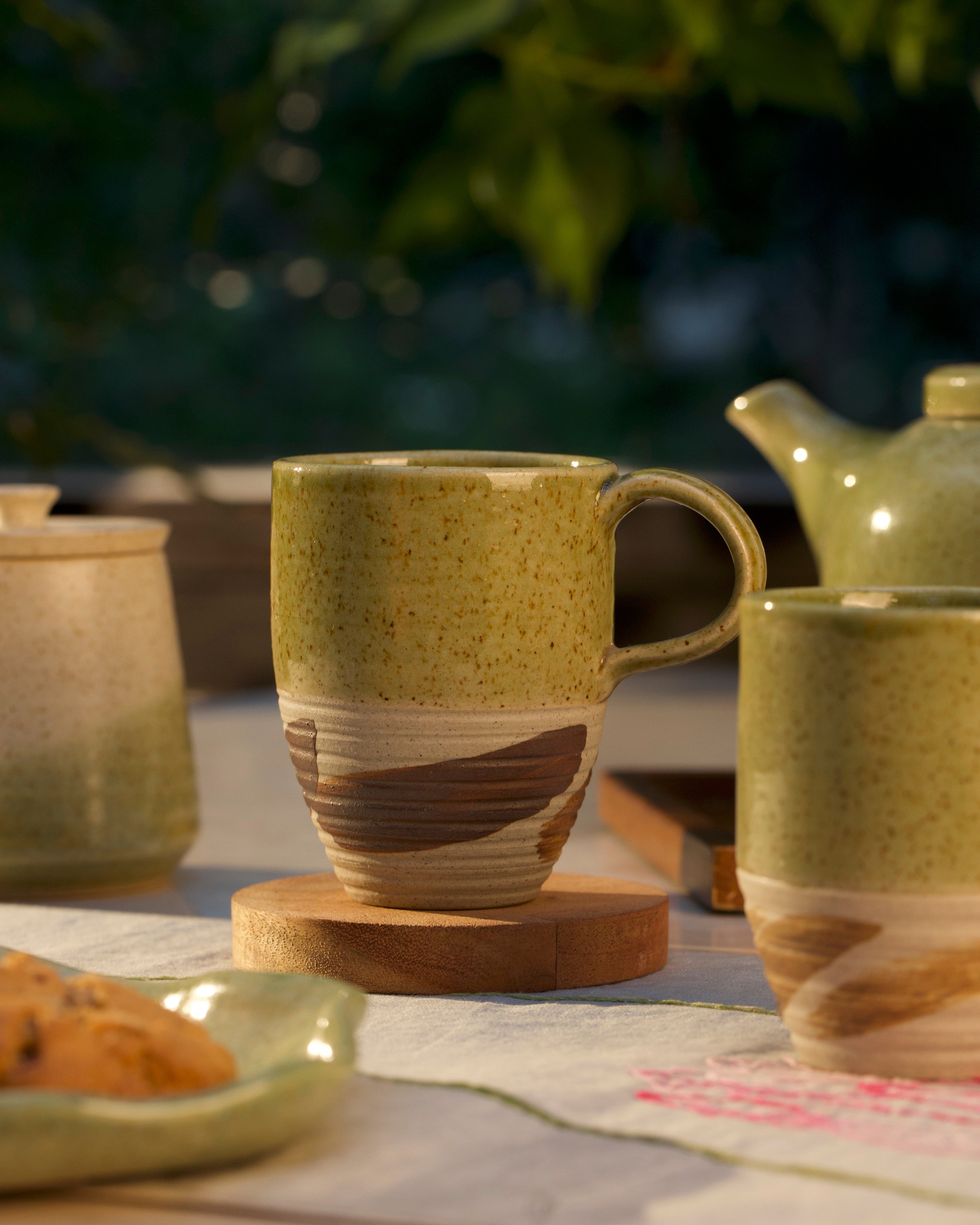 Green ceramic mug with brown accents on a wooden coaster,  ceramic coffee mugs online, handmade ceramics India
