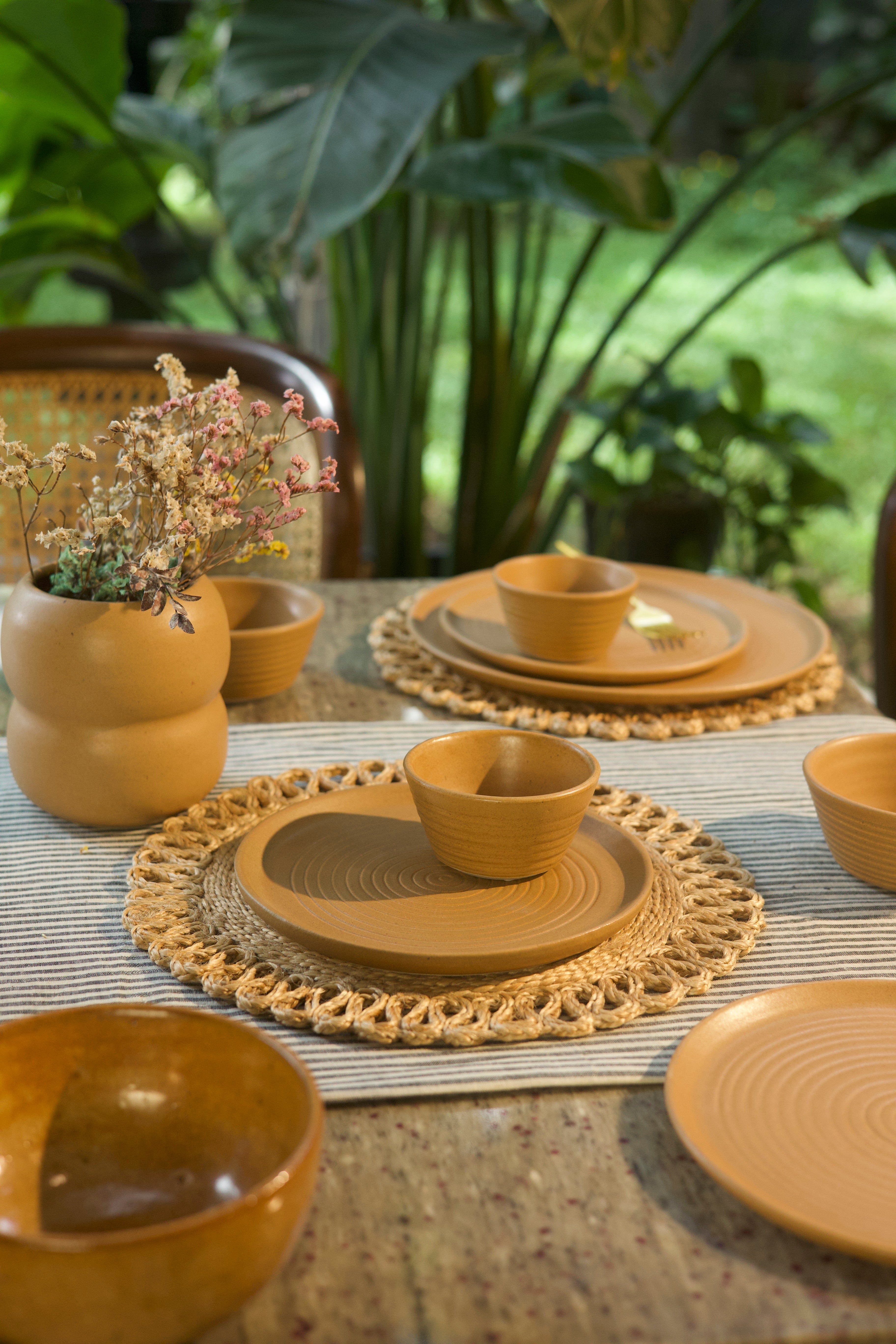 Yellow ceramic tableware set on a textured surface with plants in the background handmade dinnerware India, handcrafted plates and bowls