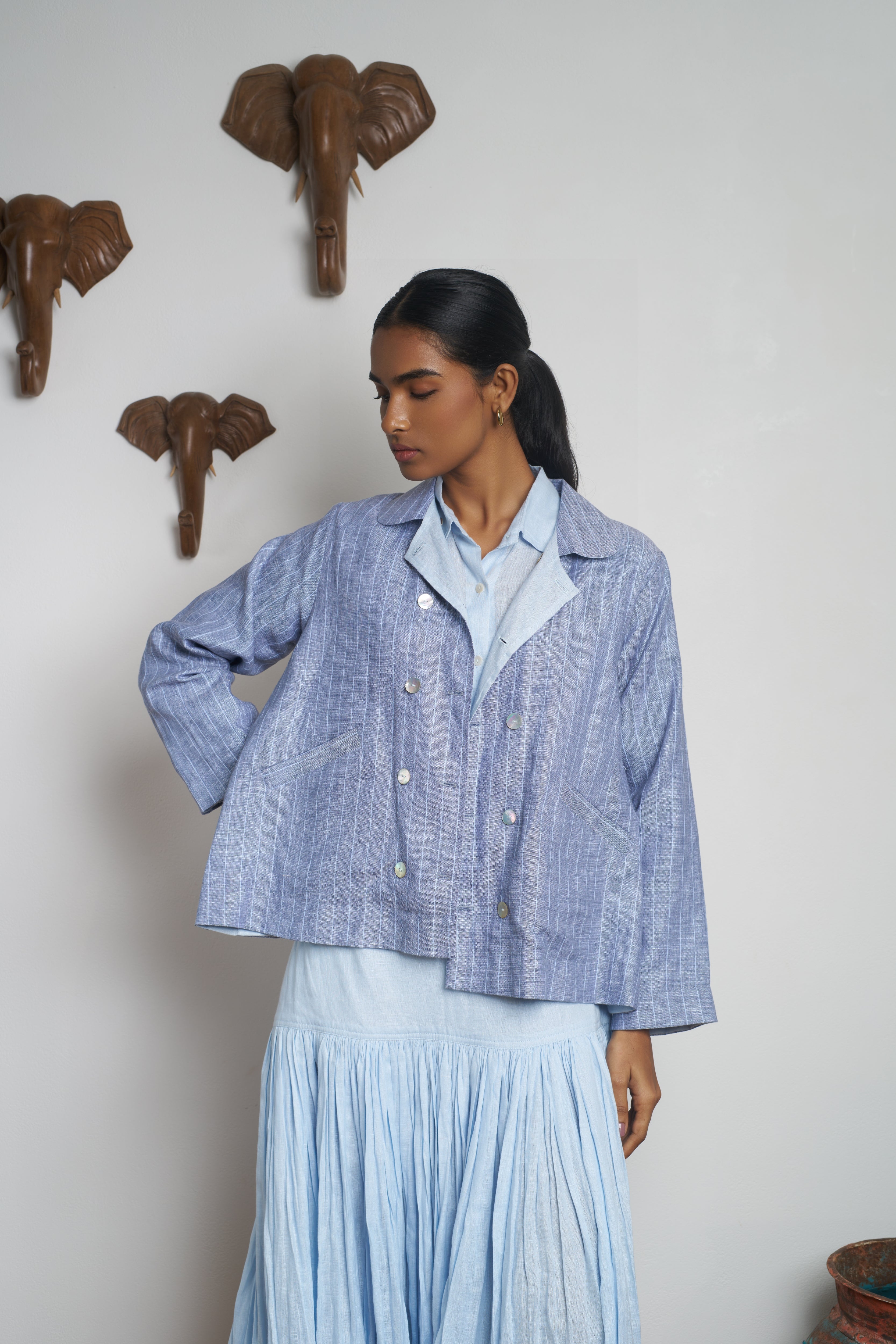 Woman wearing a blue checkered jacket and pleated skirt standing in a room. slow fashion India, everyday sustainable fashion India