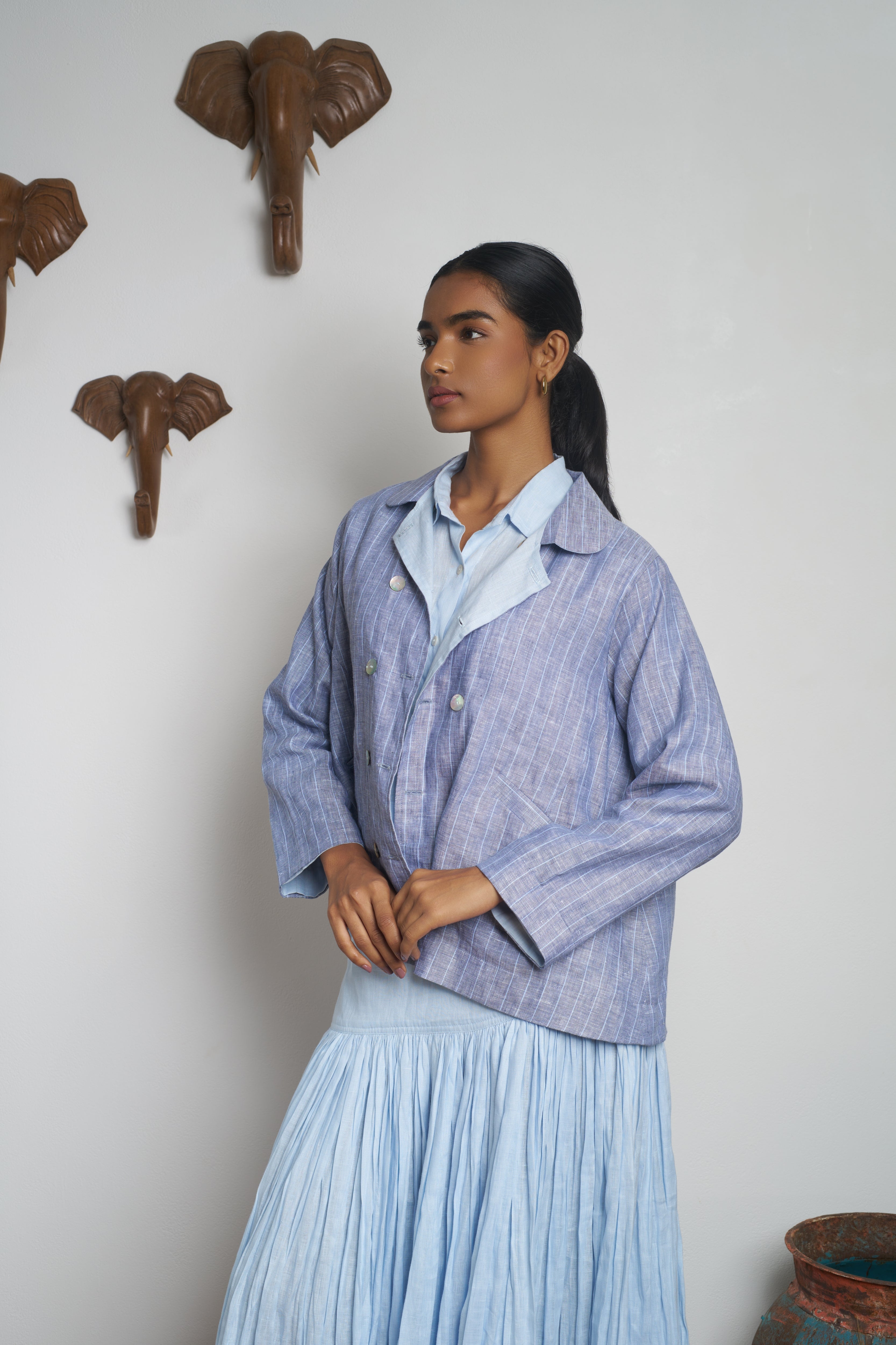 Woman wearing a blue checkered jacket and pleated skirt standing in a room. slow fashion India, everyday sustainable fashion India