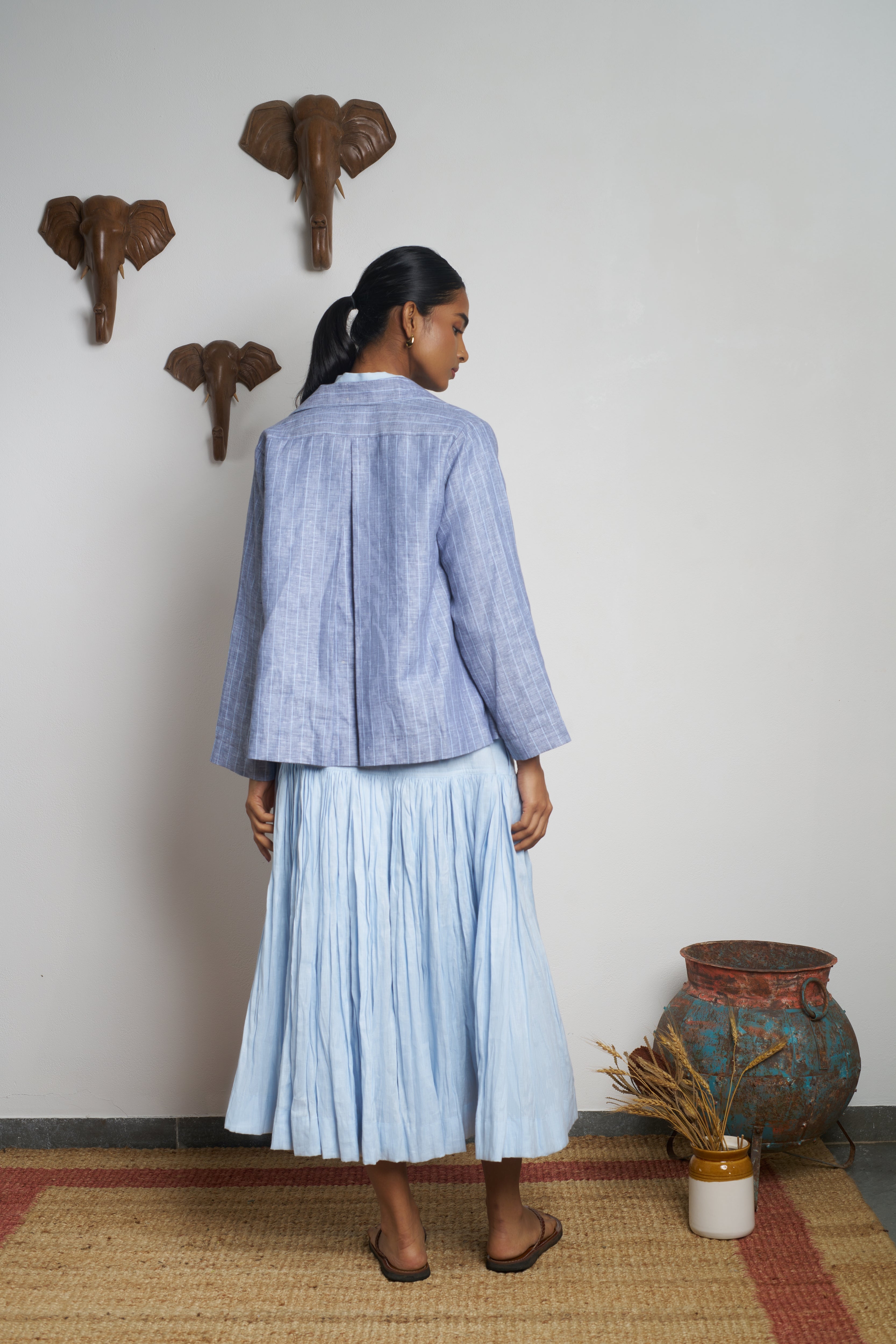 Woman wearing a blue checkered jacket and pleated skirt standing in a room. slow fashion India, everyday sustainable fashion India