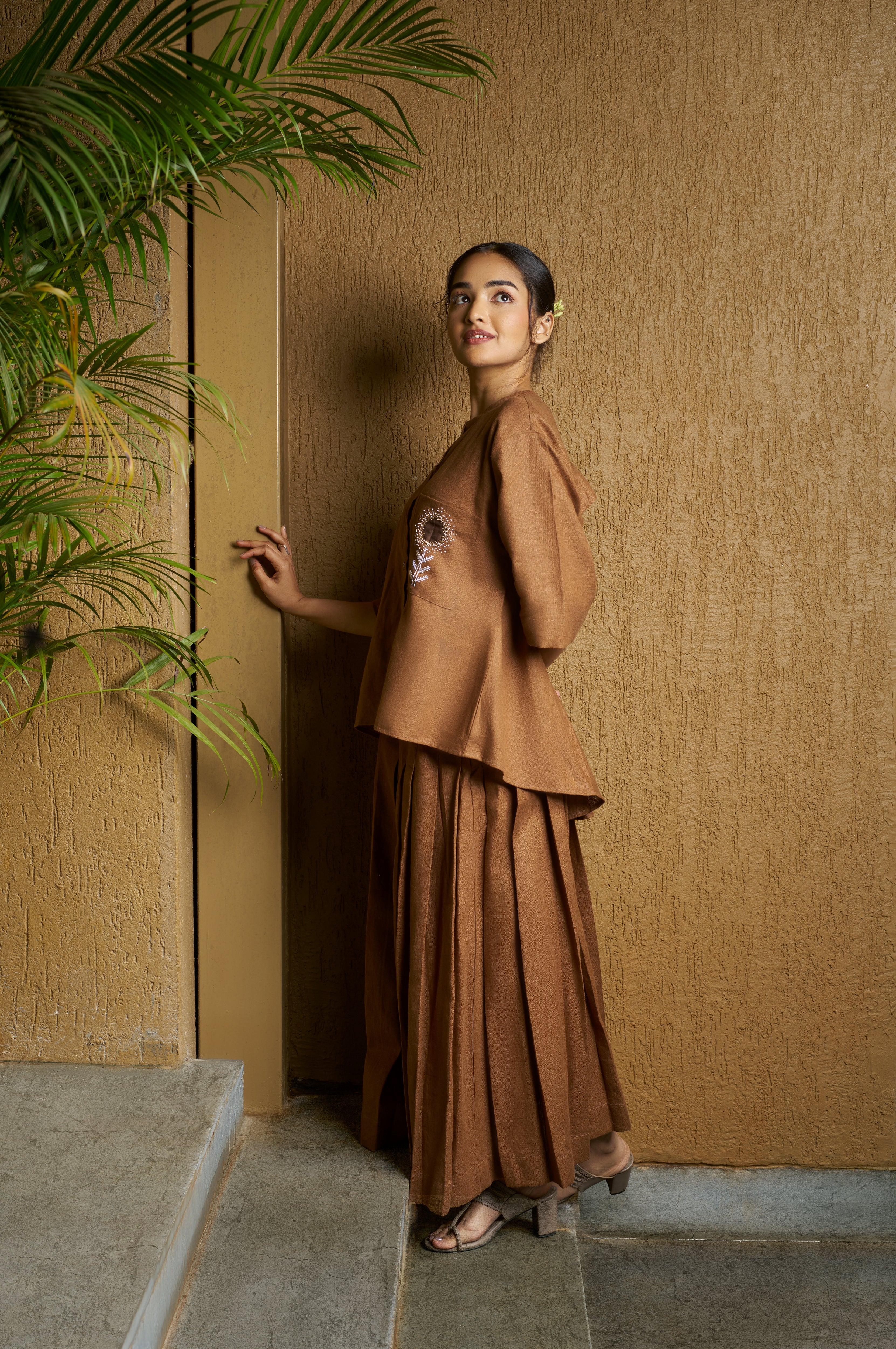 Woman in a brown blouse with embroidered white flower and brown skirt.  timeless women’s fashion, 100% linen clothes India
