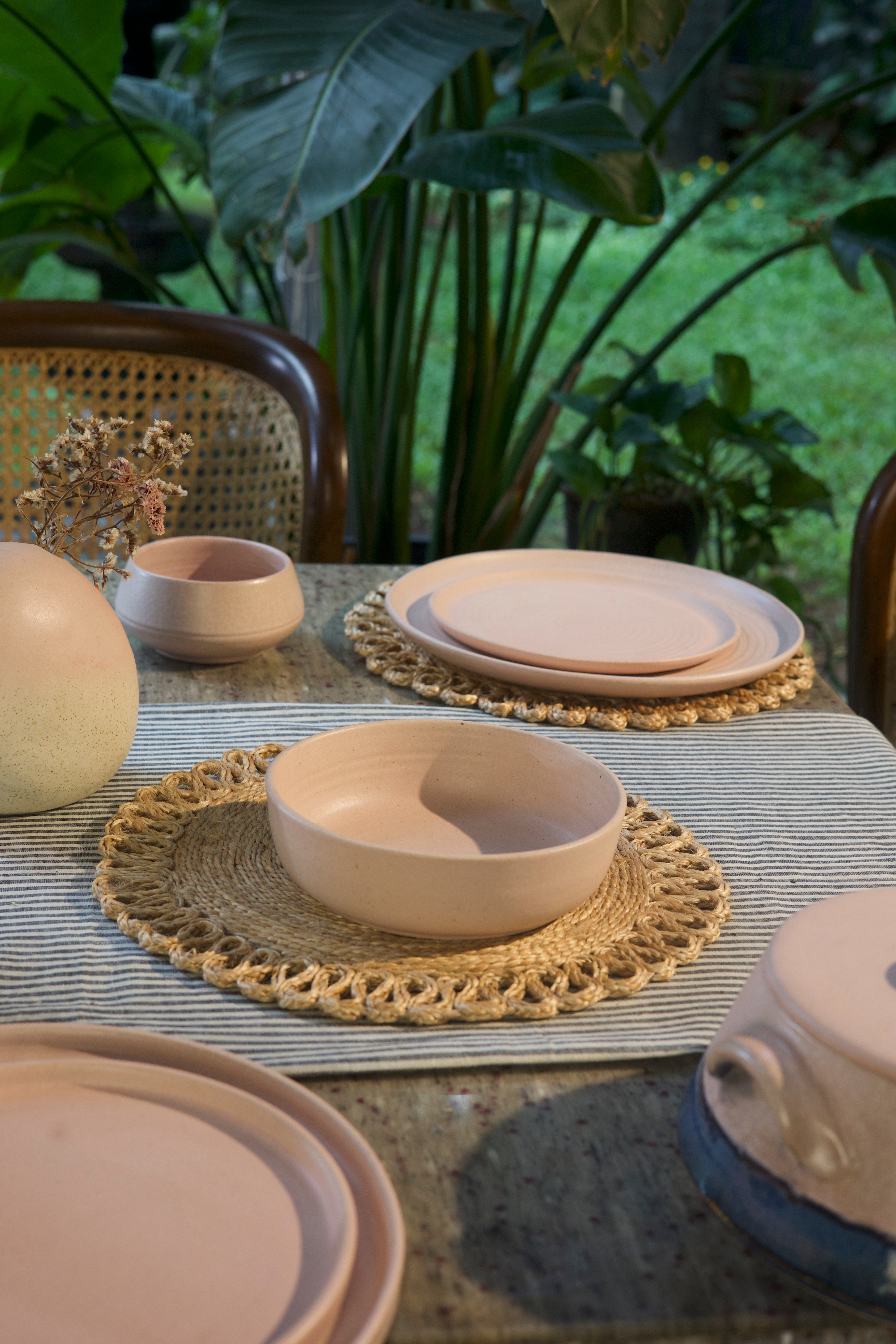 Pink ceramic bowls and plates on a table with a textured placemat, artisanal serveware India, handcrafted plates and bowls