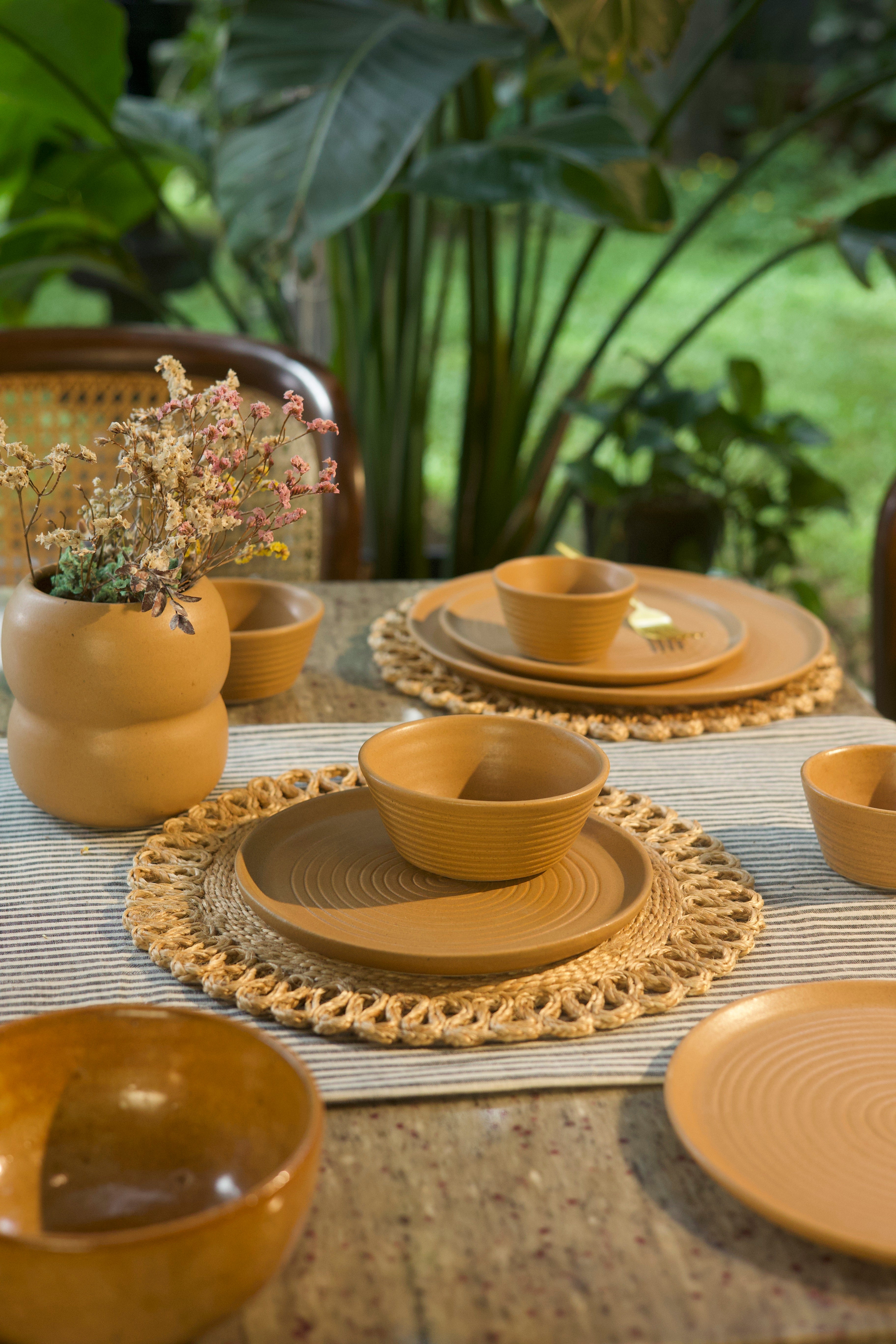 Mustard ceramic dishes on a table with woven placemats handmade dinnerware India, handcrafted plates and bowls