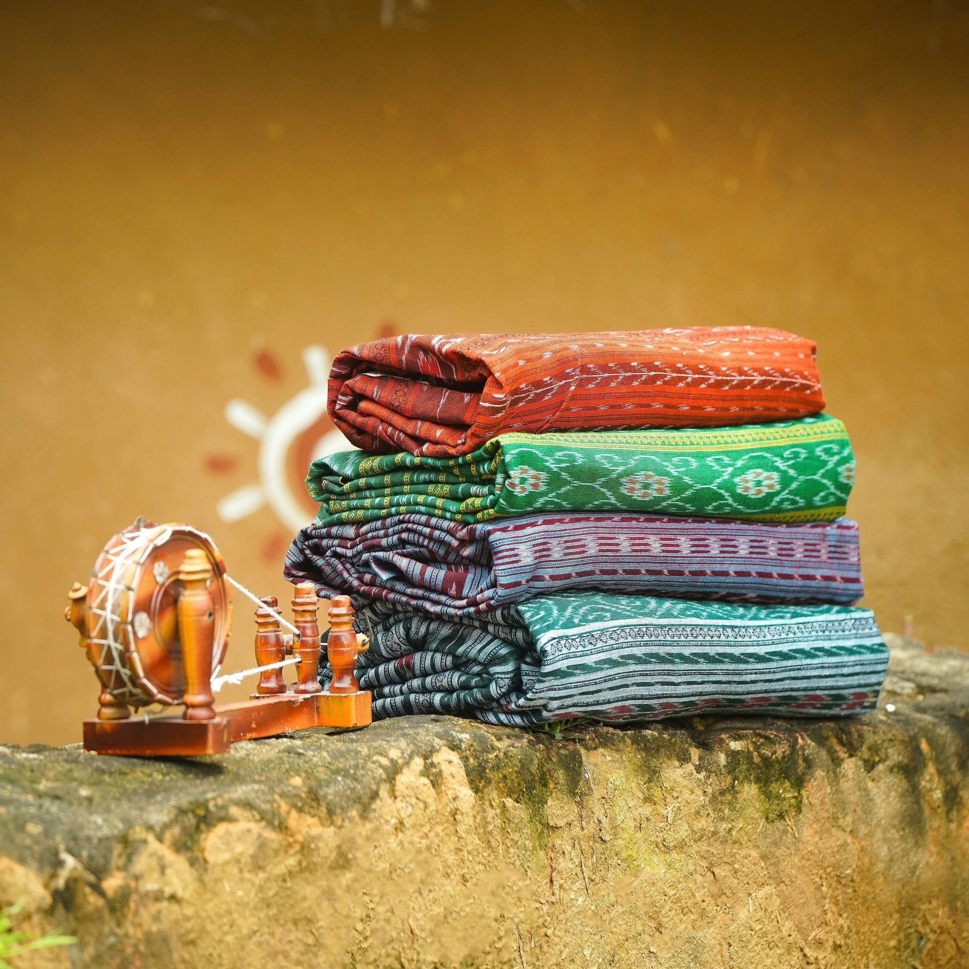 Stack of colorful fabric rolls on a stone surface with a thatched roof,  organic materials India, circular design practices