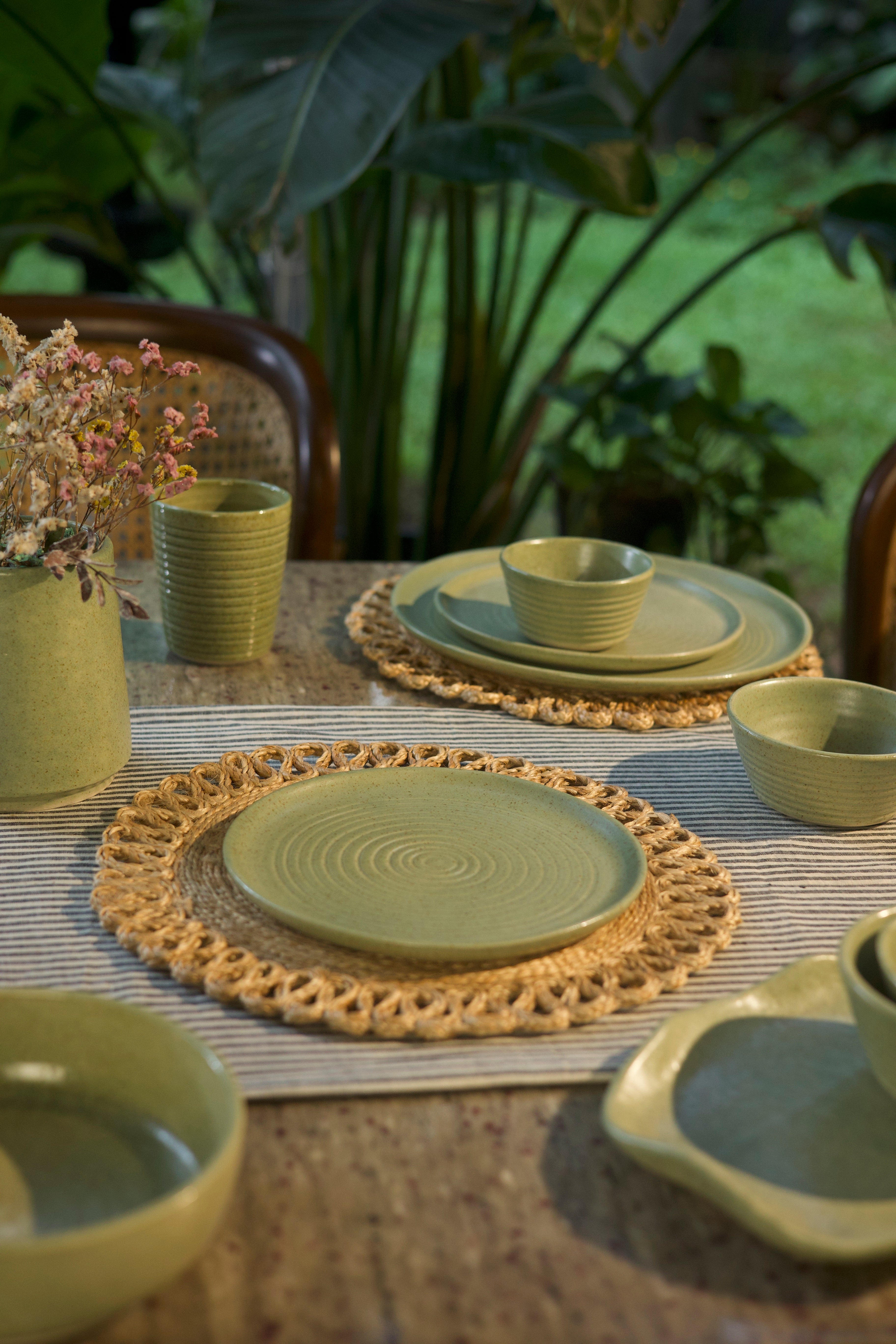 Green ceramic tableware set on a textured surface,  handmade dinnerware India, handcrafted plates and bowls