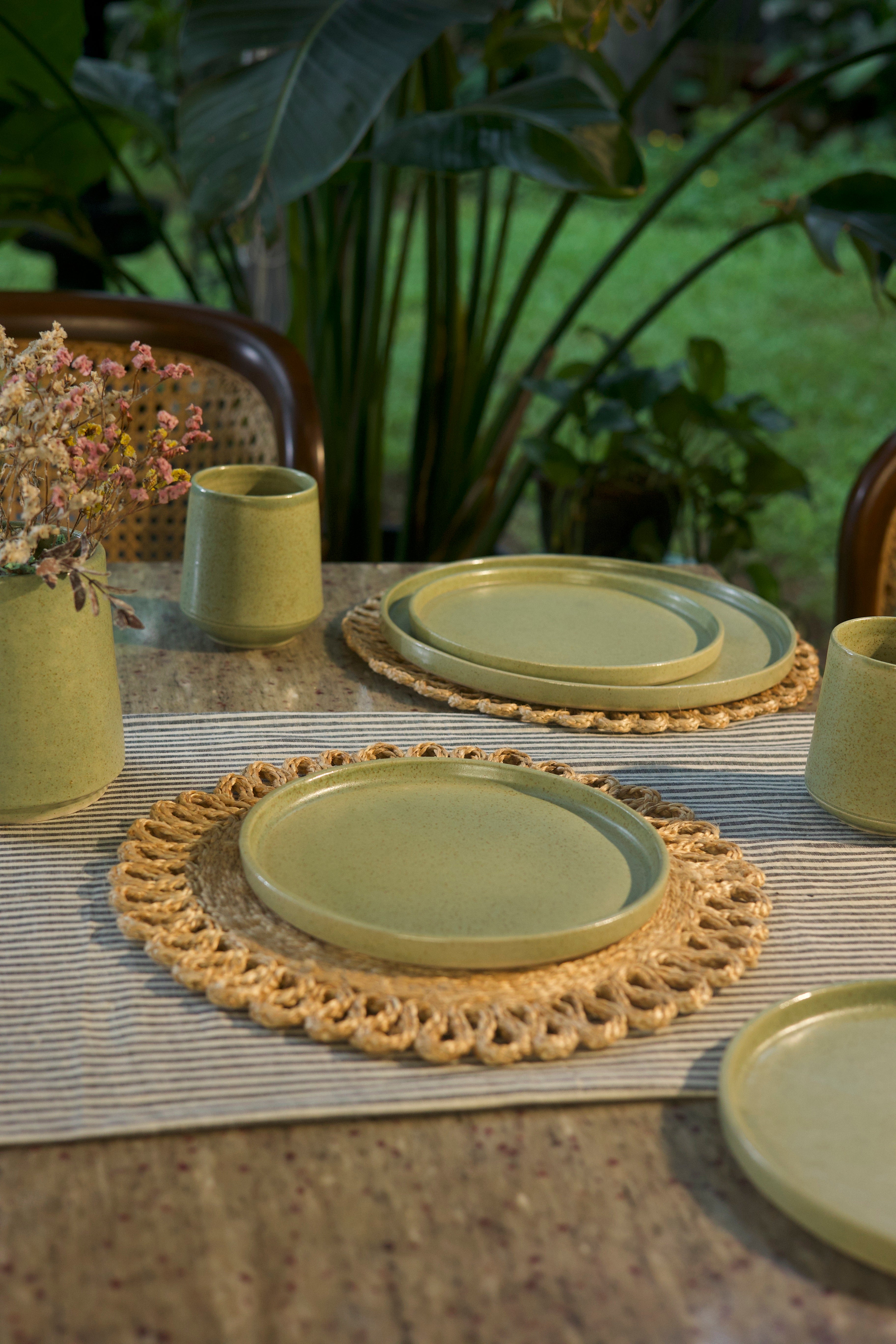 Green ceramic plates and cups on a table with a woven placemat,  handmade dinnerware India, handcrafted plates and bowls