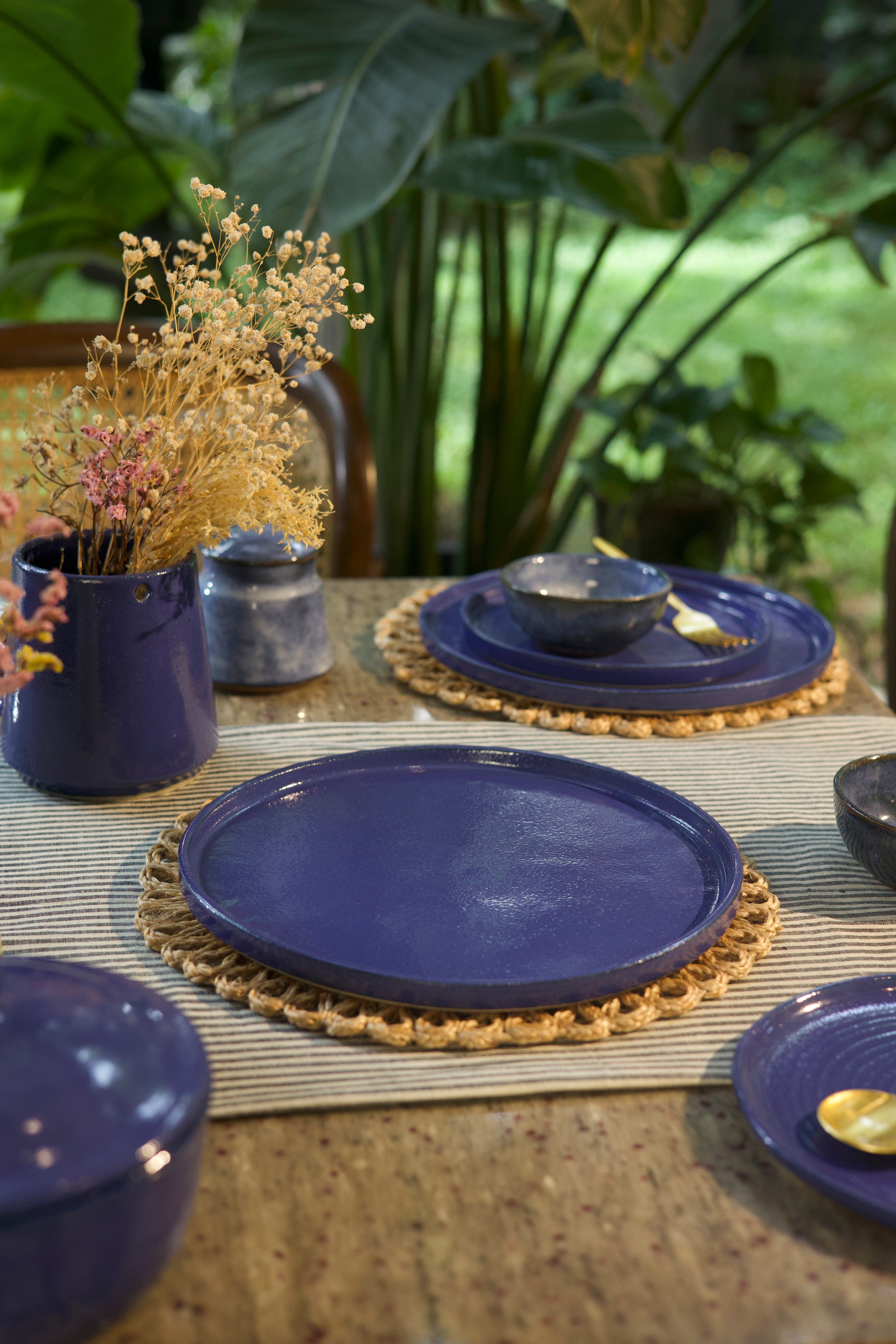 Navy blue plates on a table with decorative elements and plants in the background, handmade dinnerware India, handcrafted plates and bowls