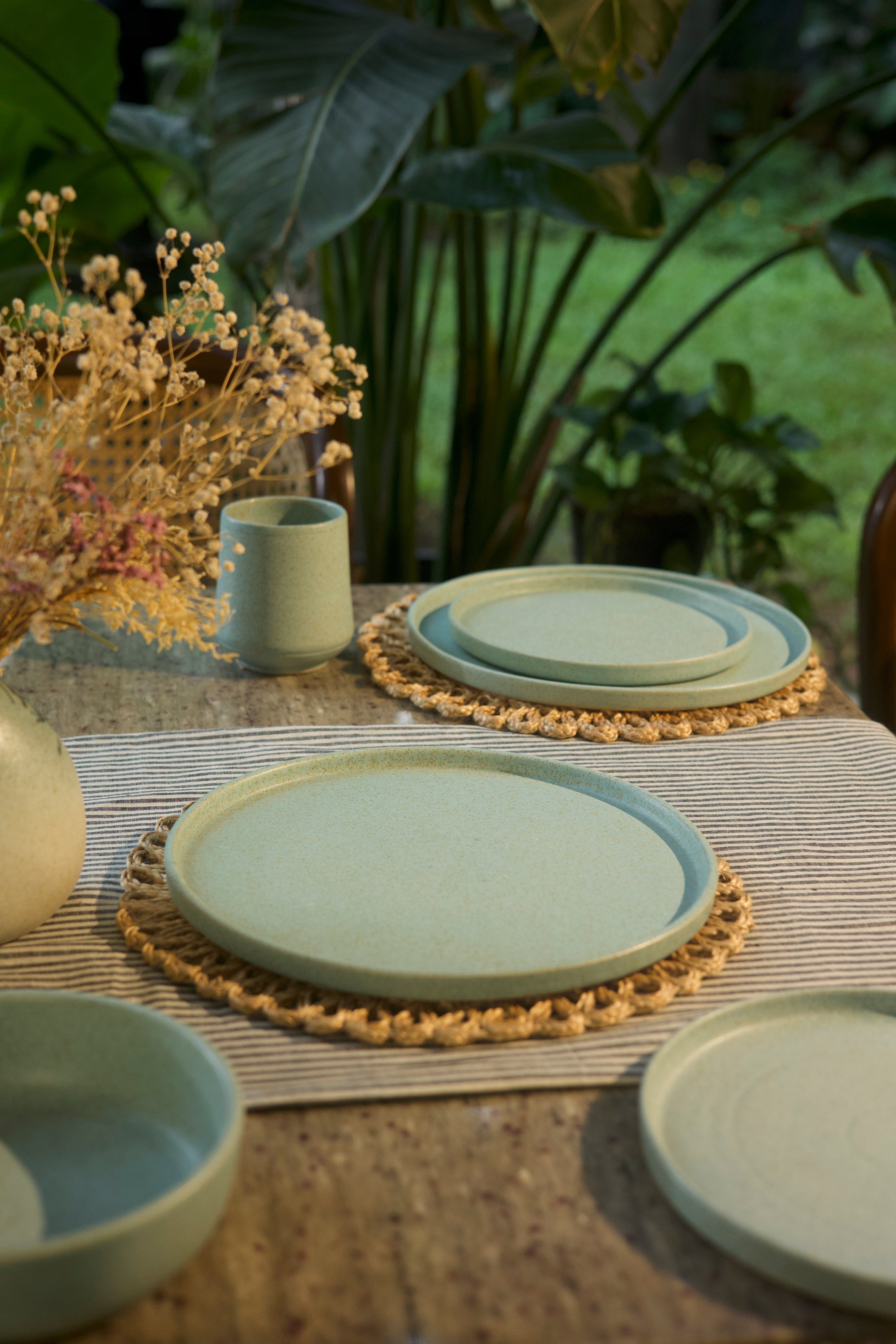 Set of green ceramic plates on a textured surface , handmade dinnerware India, handcrafted plates and bowls