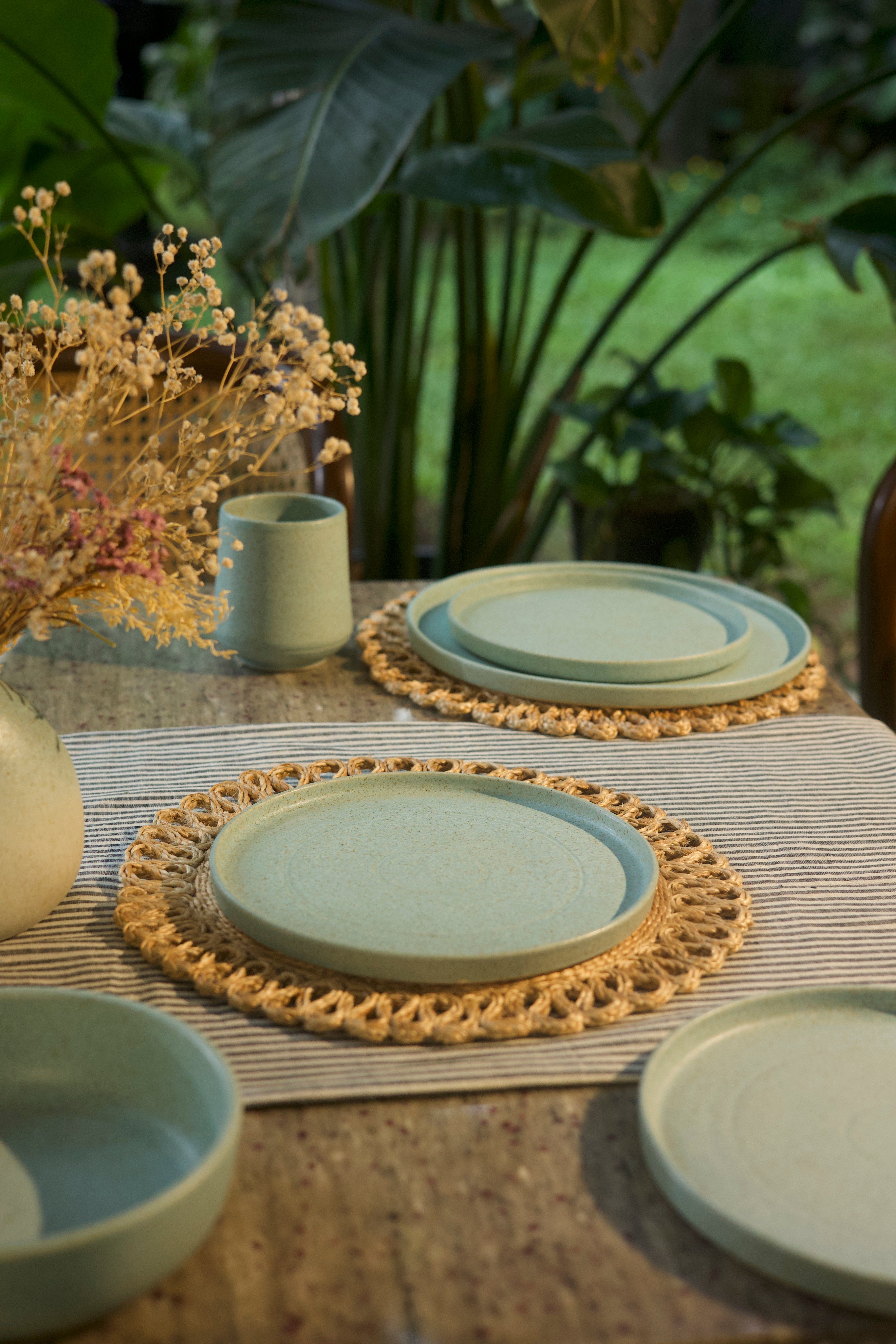 Set of green ceramic plates and cups on woven placemats  handmade dinnerware India, handcrafted plates and bowls