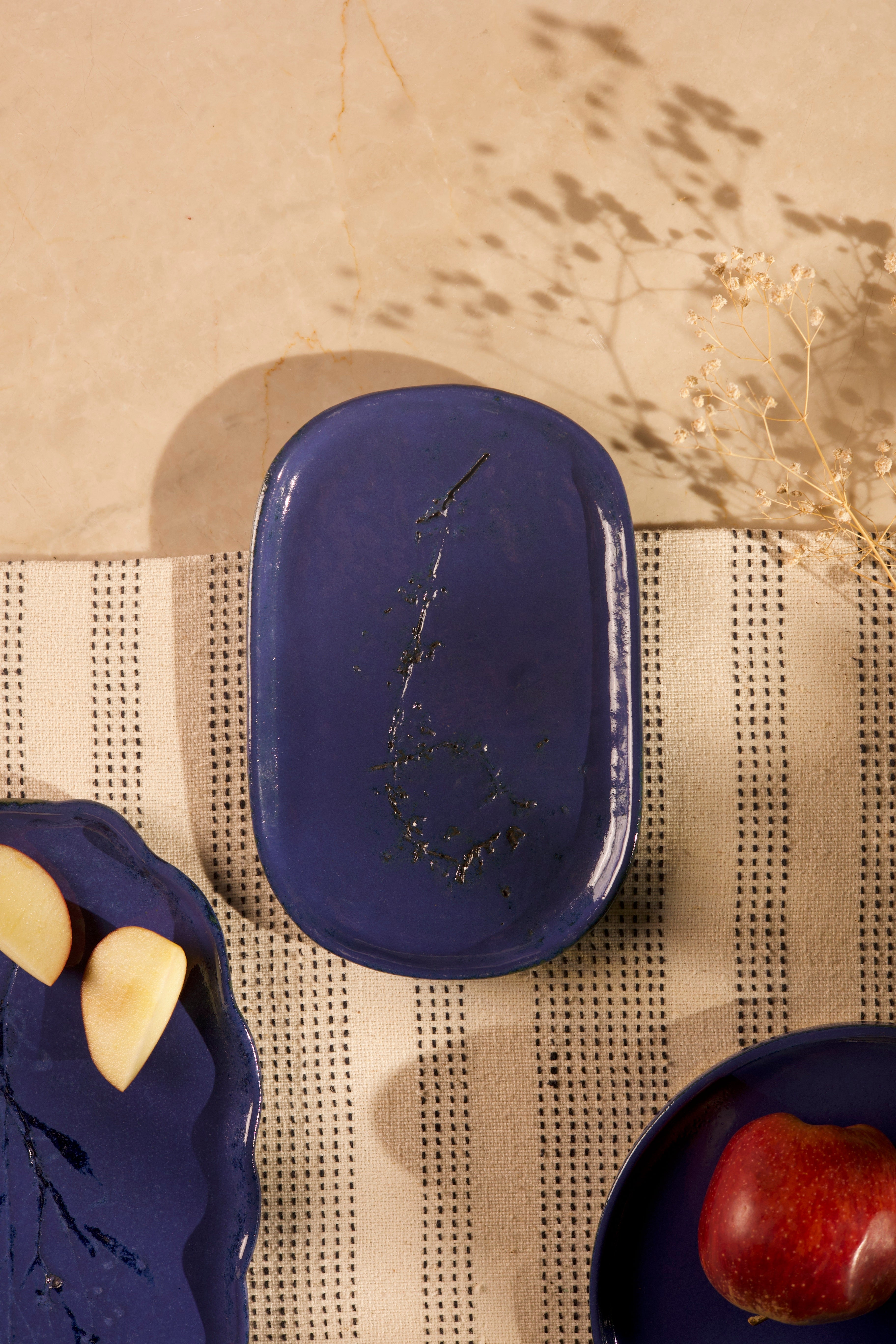 Blue ceramic dish on a textured surface with a plant in the background handcrafted plates and bowls, dinner plates with natural glaze
