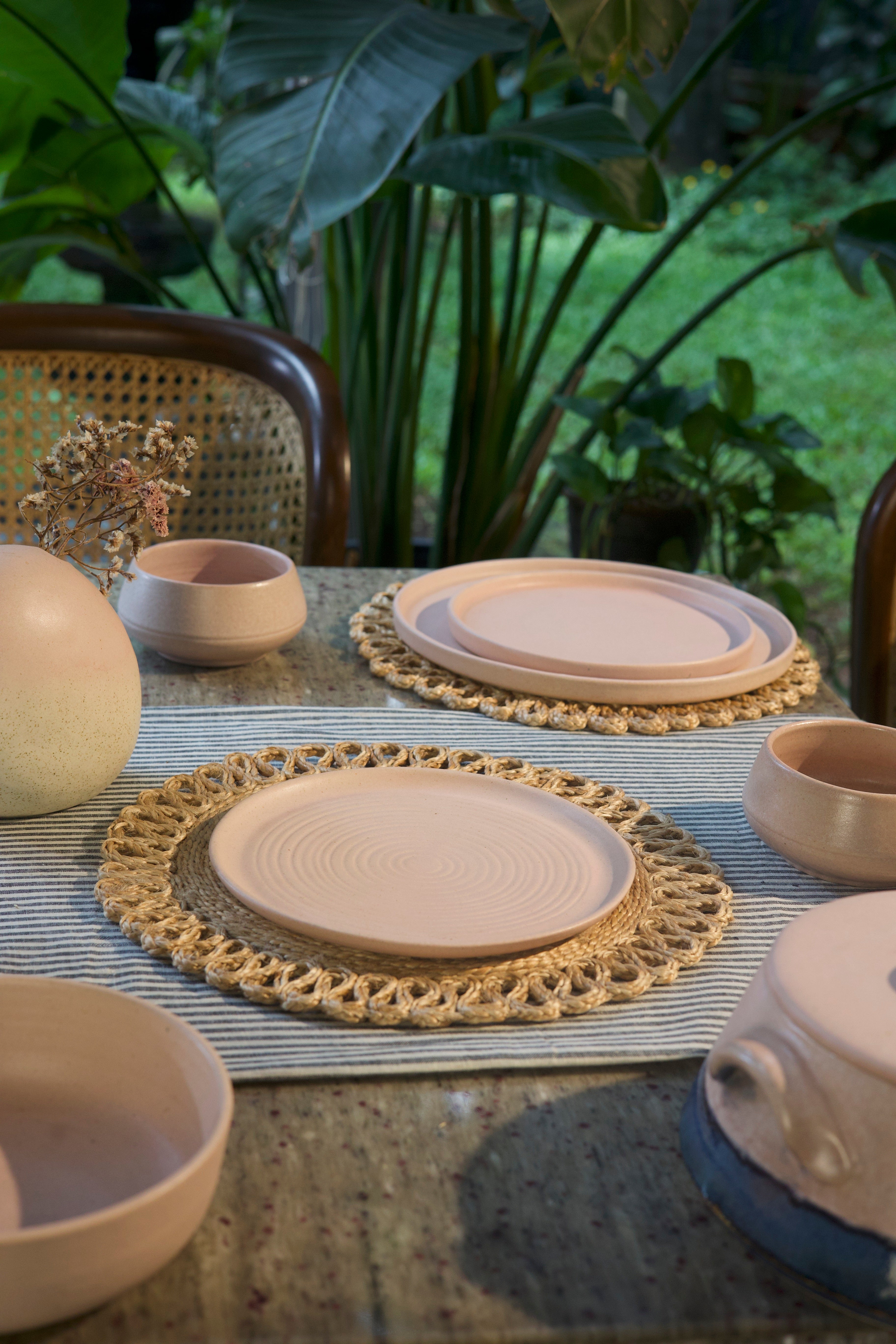Ceramic plates and bowls on a table with a woven placemat, handmade dinnerware India, handcrafted plates and bowls