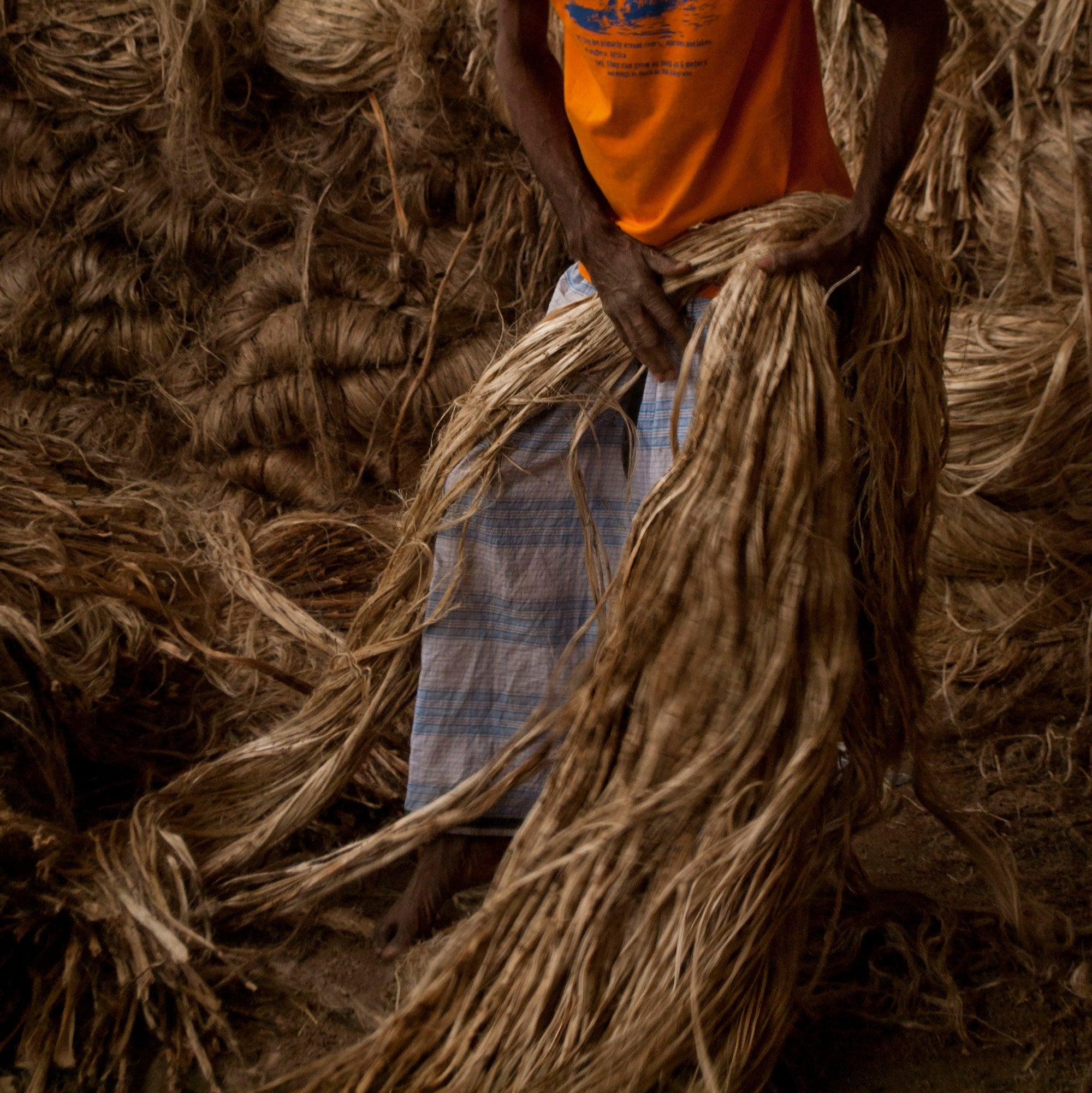 Person wearing an orange shirt amidst stacks of straw or hay,  organic materials India, circular design practices
