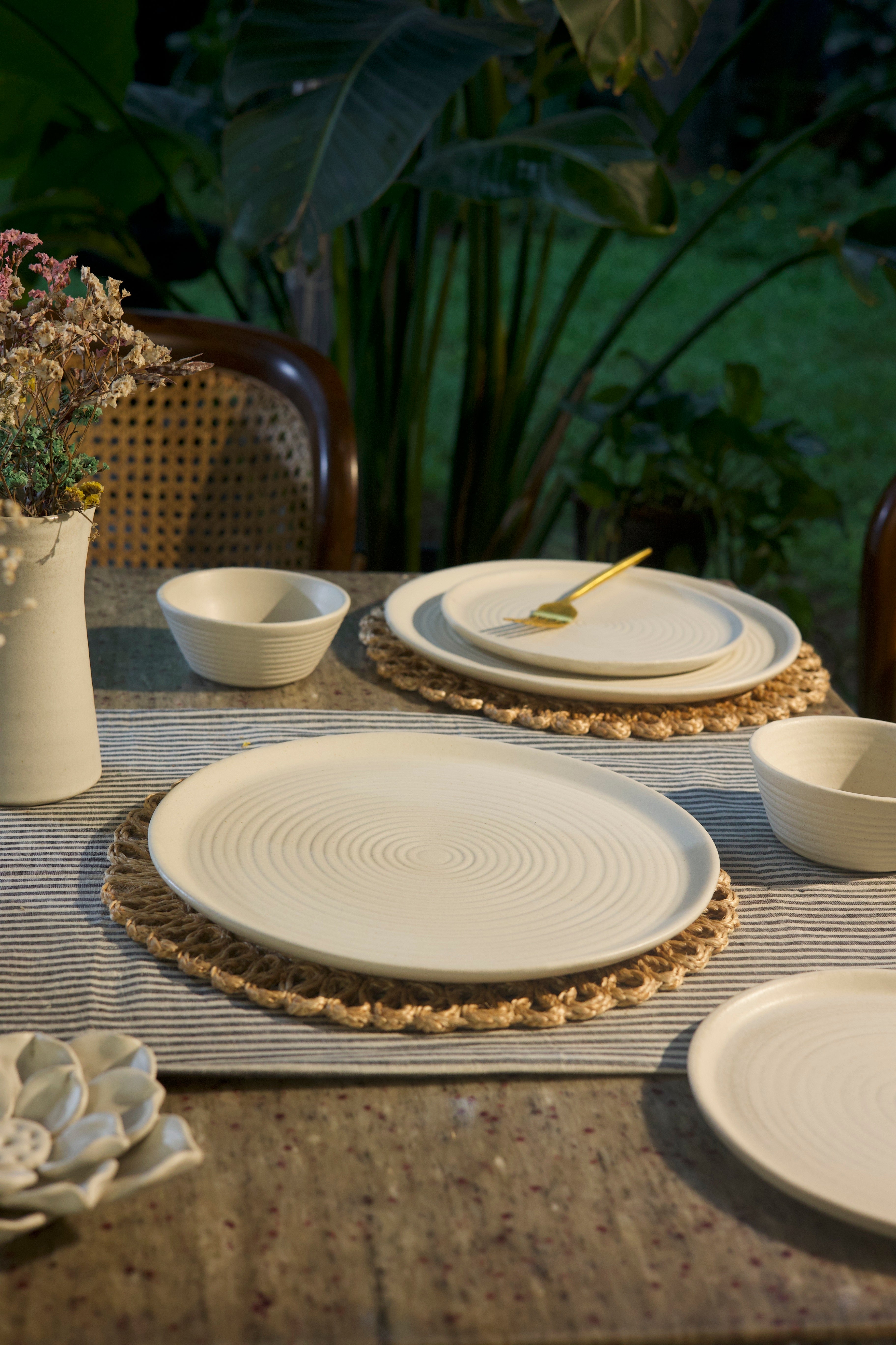 White ceramic plates and bowls on a textured surface.  handmade dinnerware India, handcrafted plates and bowls